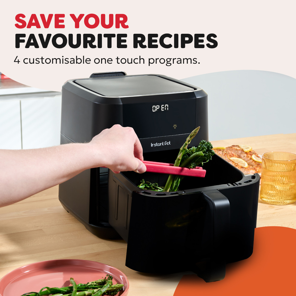 Ręka używa czerwonych szczypiec do wkładania szparagów i brokułów do czarnej frytkownicy beztłuszczowej Instant Pot.