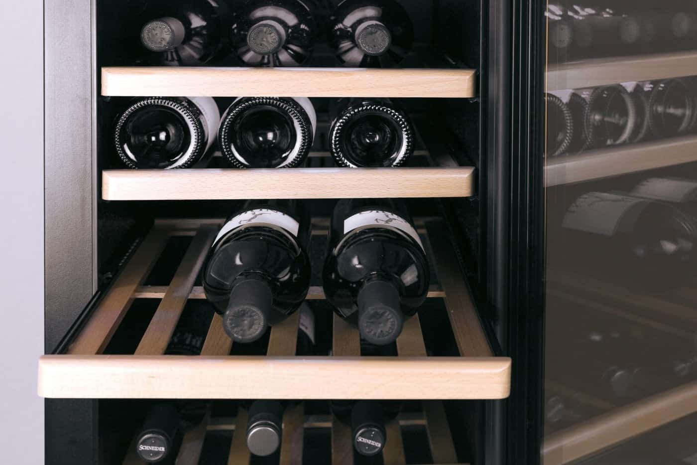 Una cantinetta per vini con ripiani in legno che ospitano molte bottiglie di vino scure.