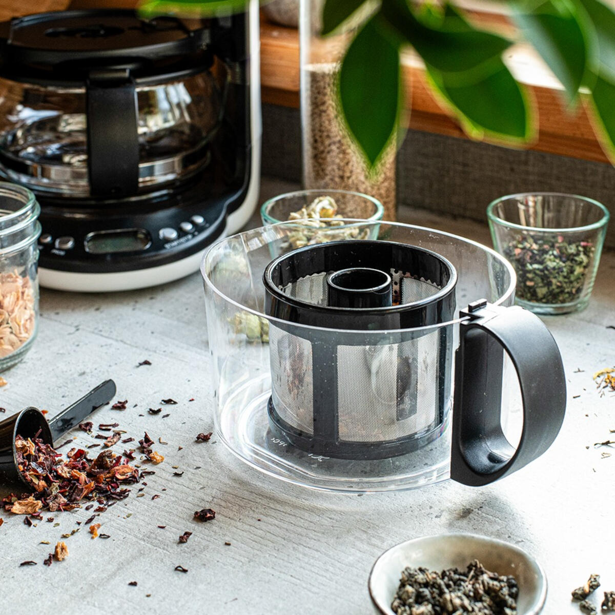 Eine Kaffeemaschine, ein Teefilter und Schalen mit getrocknetem Tee auf einer Arbeitsplatte.