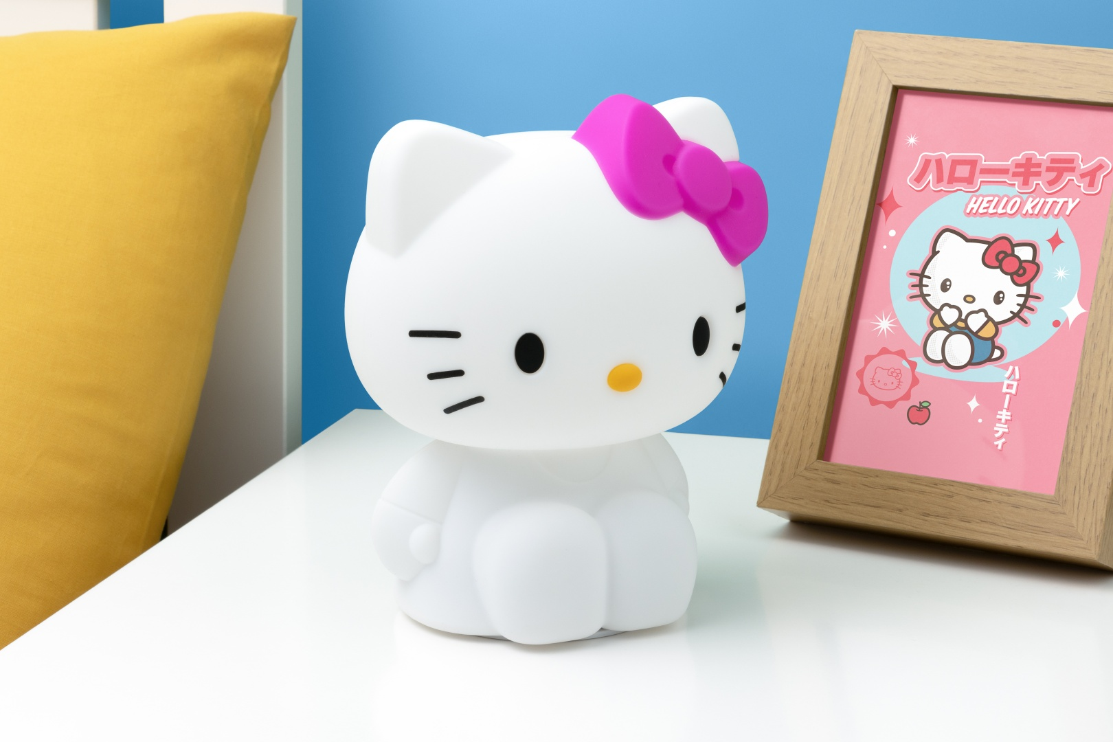 Eine weiße Hello-Kitty-Lampe mit pinker Schleife steht neben einem Bilderrahmen mit Hello Kitty.