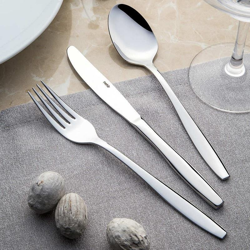 Gri kumaş üzerinde parlak metal çatal bıçak seti, ceviz ve tabak ile.