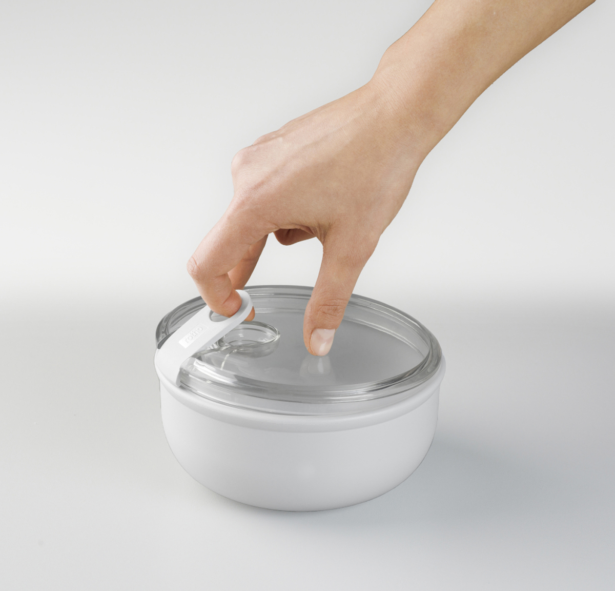 Una mano apre un contenitore bianco con coperchio trasparente.