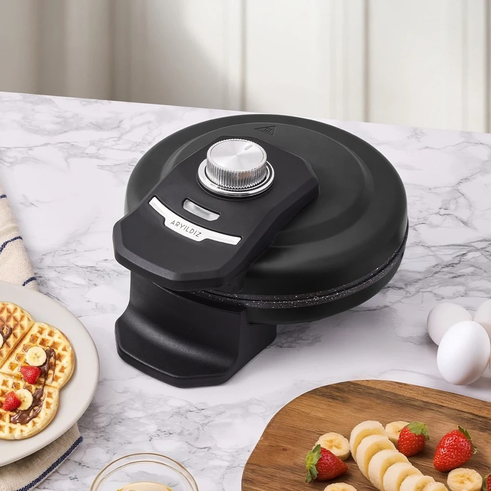 Gümüş kadranlı siyah waffle makinesi. Mermer tezgahta waffle, meyve ve yumurta.