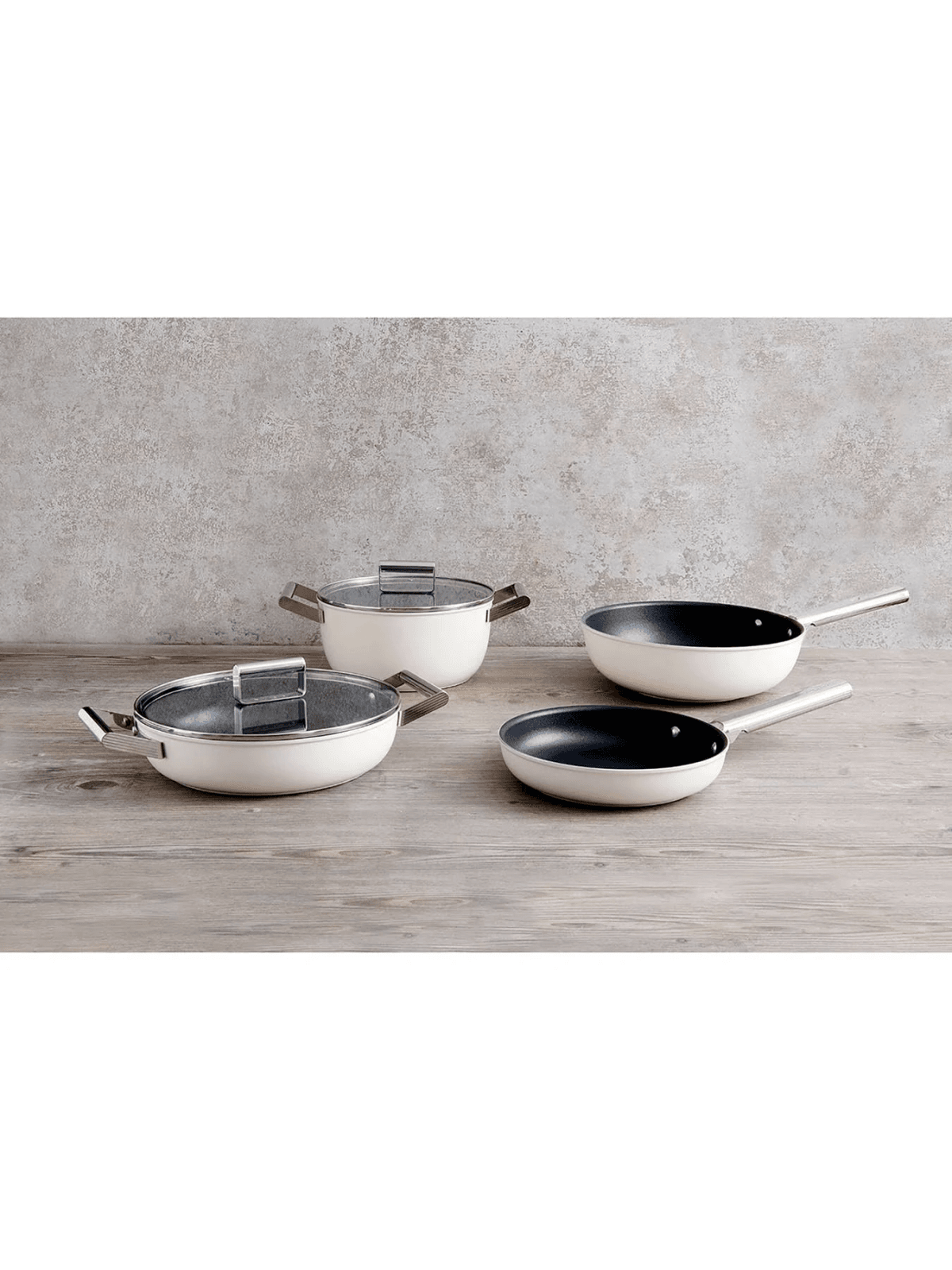 Cuatro utensilios de cocina blancos sobre mesa de madera: dos ollas con tapa, dos sartenes.