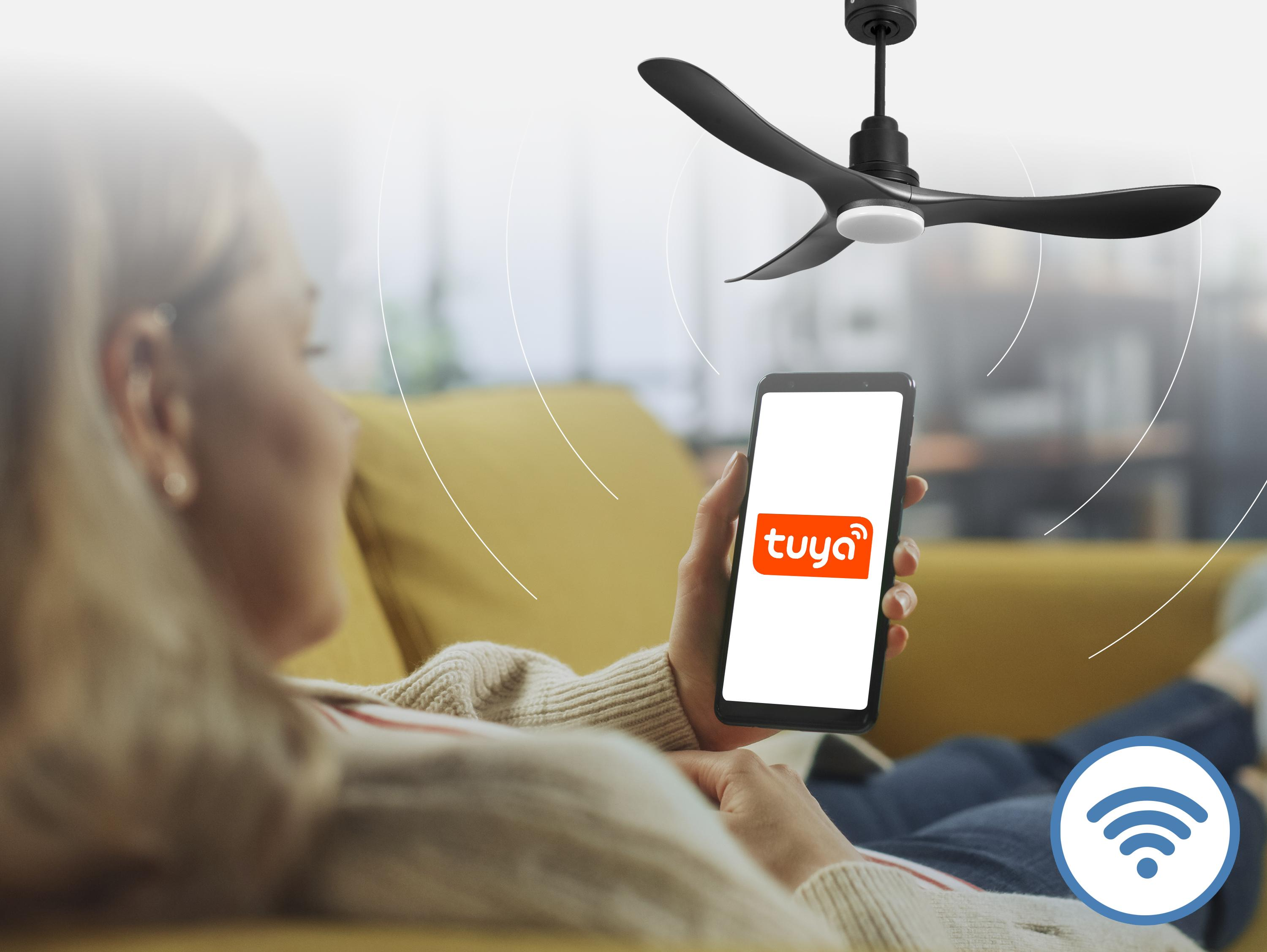 Una mujer en un sofá usa un smartphone con la app Tuya. Se ve un ventilador de techo.