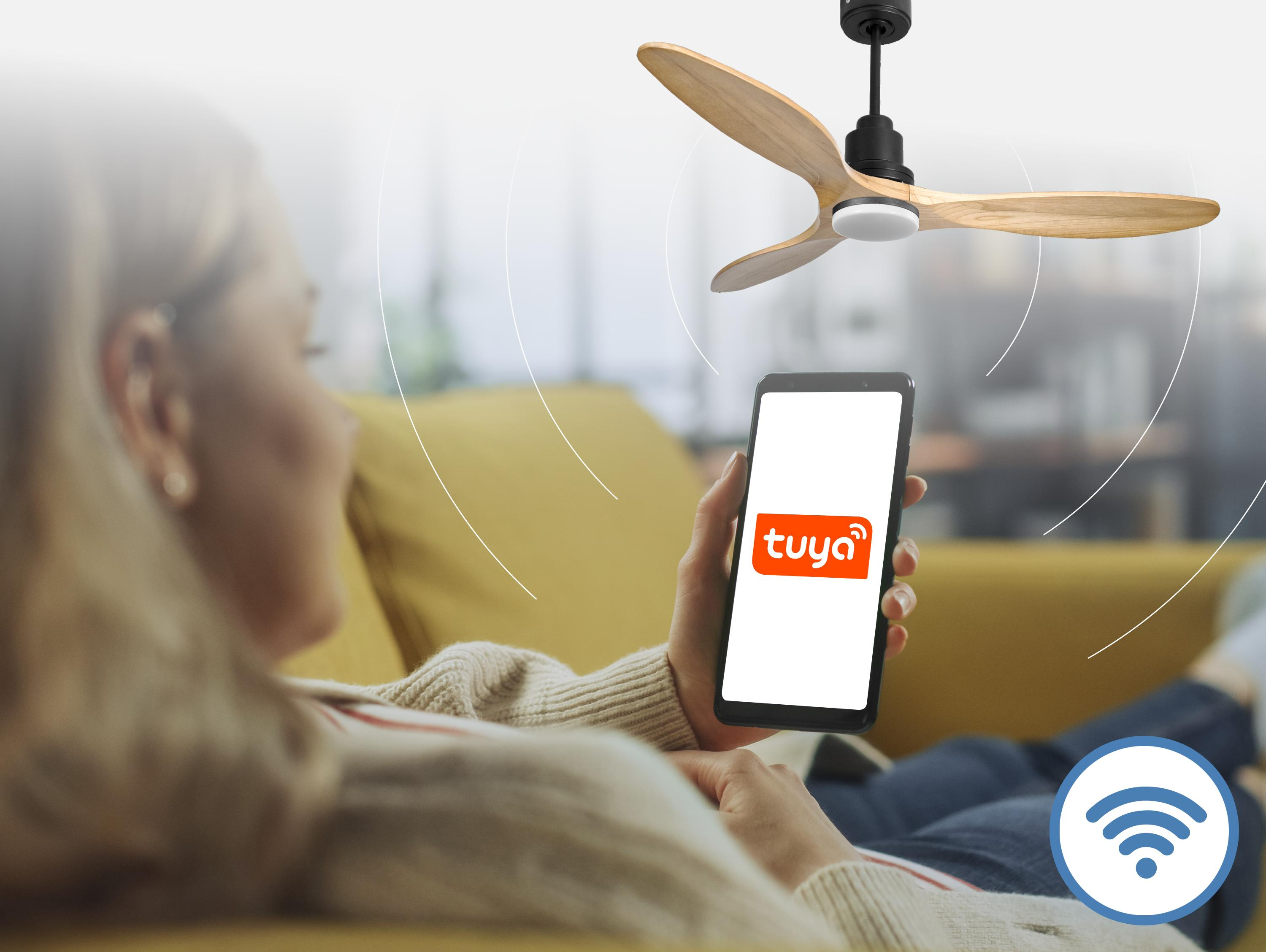 Una mujer en un sofá usa su teléfono para controlar un ventilador de techo.