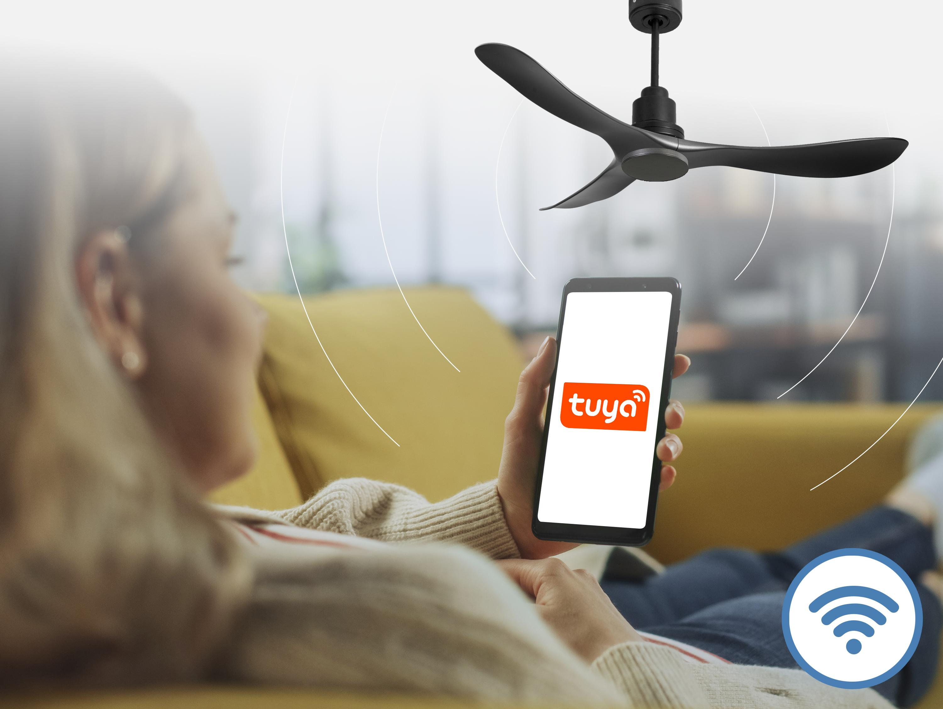 Una mujer yace en un sofá, controlando un ventilador de techo con su smartphone.