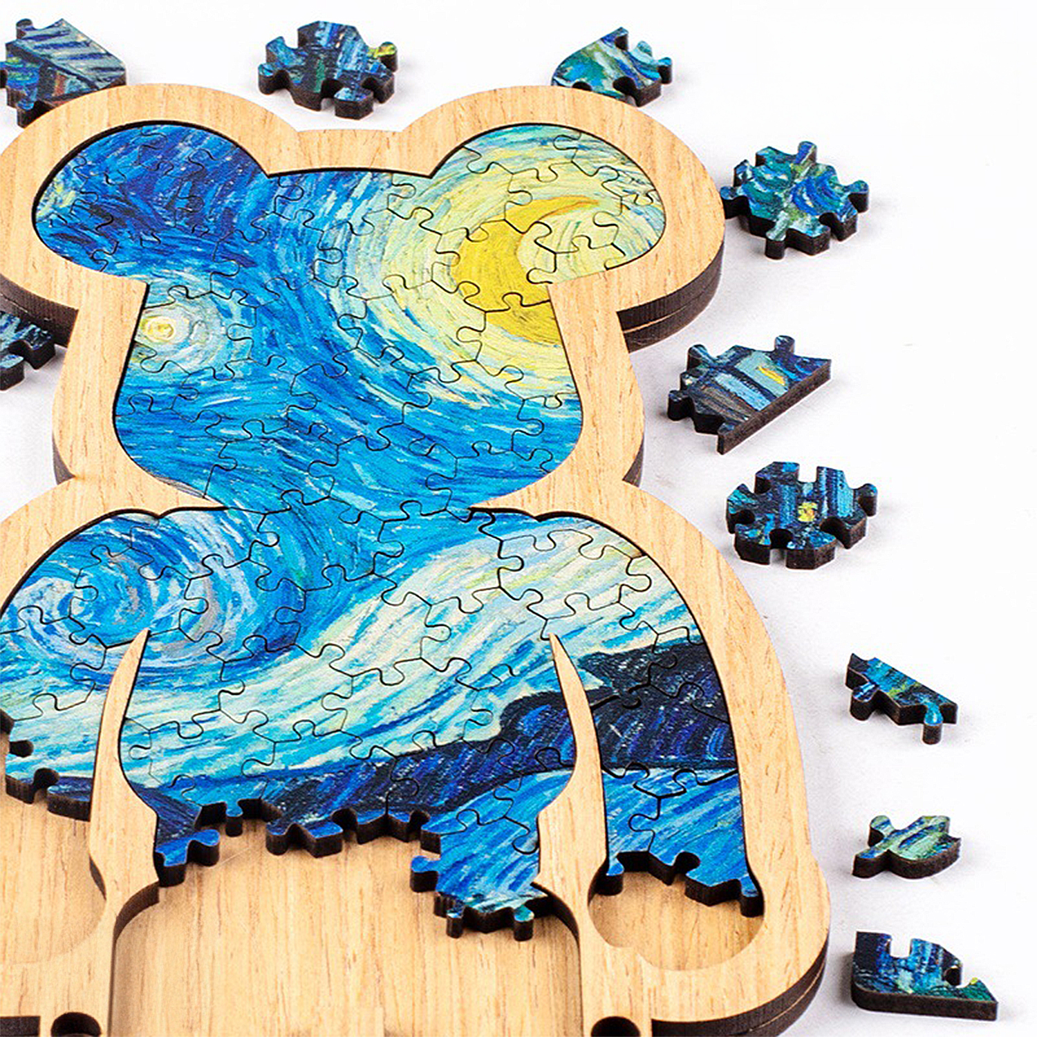 Un puzzle in legno a forma di orso raffigurante La notte stellata di Van Gogh, con pezzi sparsi.