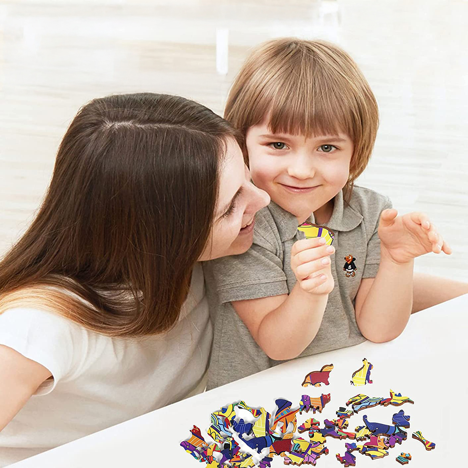 Donna e bambino giocano con pezzi di puzzle in legno colorati su un tavolo bianco.