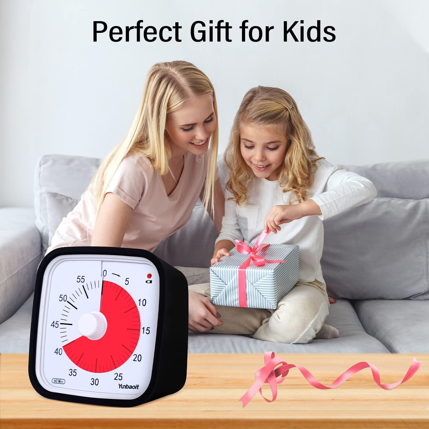 Eine Frau und ein Kind öffnen ein Geschenk auf einem Sofa, neben einem schwarzen Timer.