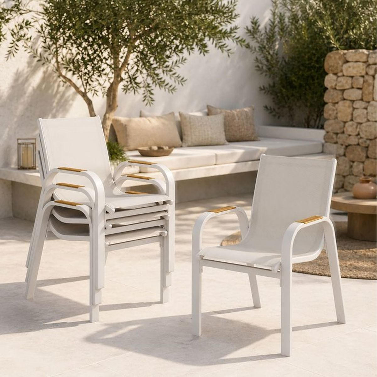 Weiße Stapelstühle mit Holzdetails auf einer sonnigen Terrasse mit Sitzbank und Olivenbaum.