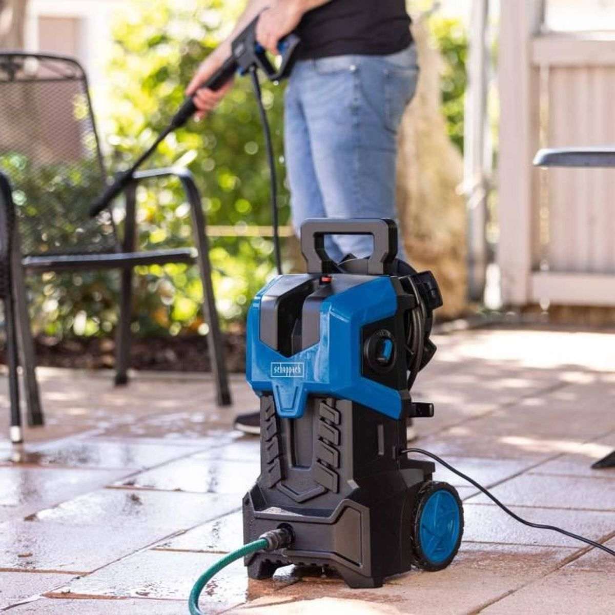 Ein Mann reinigt einen Gartenstuhl mit einem Hochdruckreiniger. Blaue und schwarze Maschine.