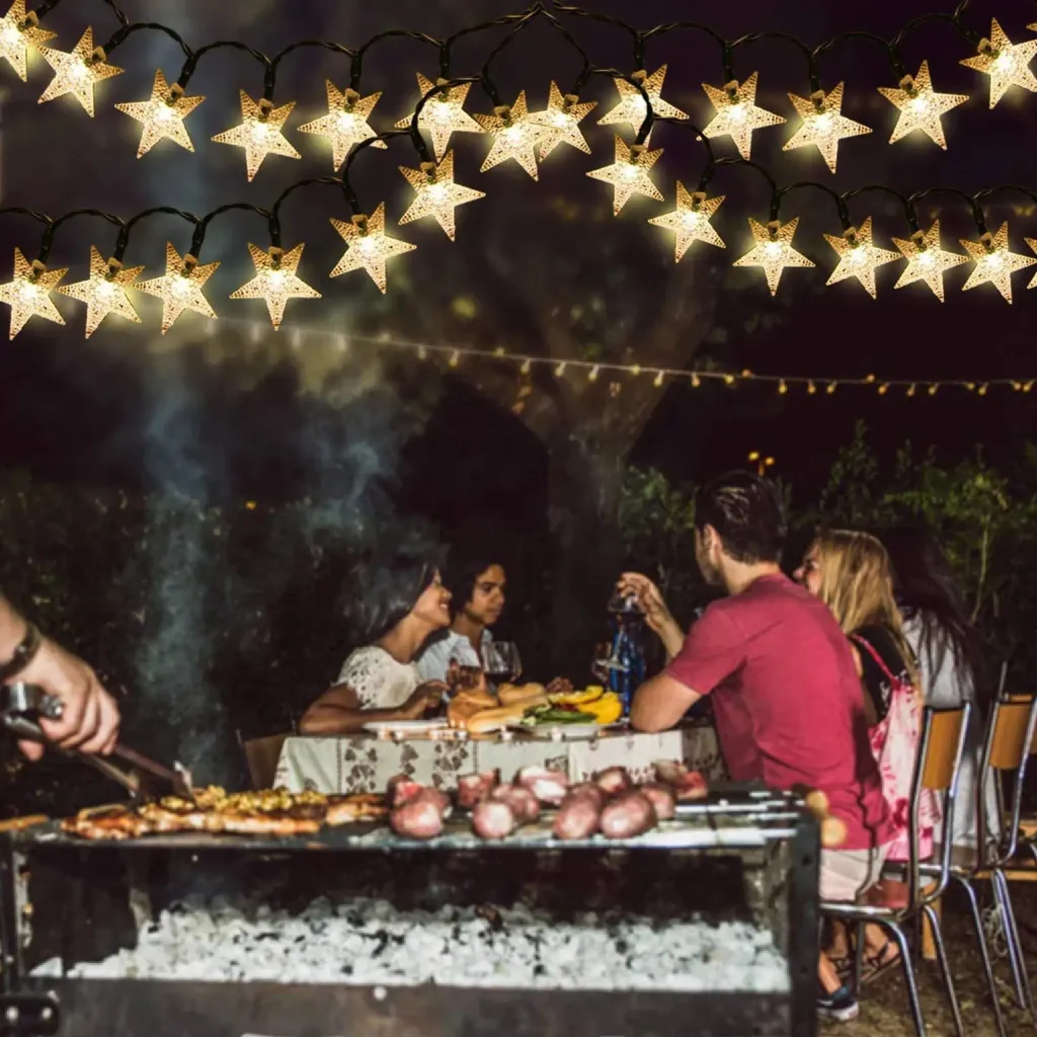 Menschen genießen ein Nacht-BBQ mit sternförmigen Lichtern darüber.