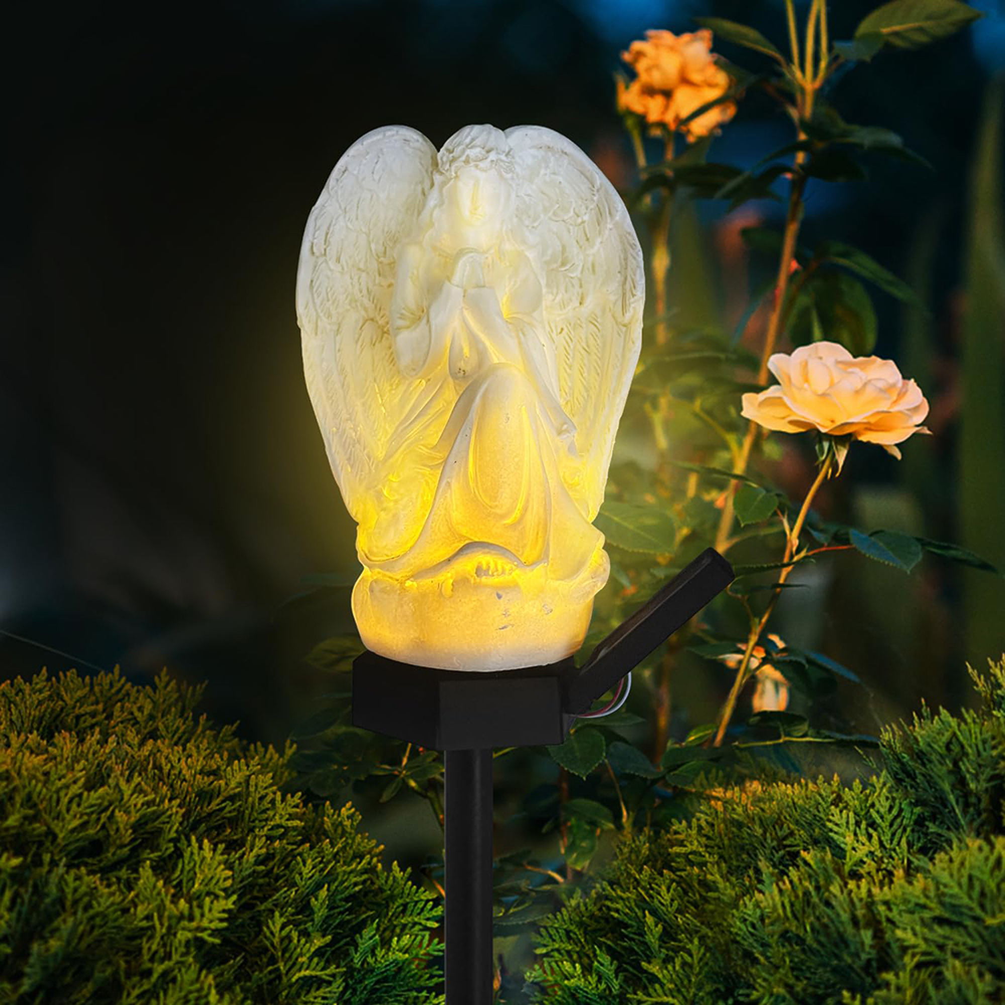 Weiße Engelsfigur mit Solarlicht leuchtet gelb in einem Garten mit Rosen.