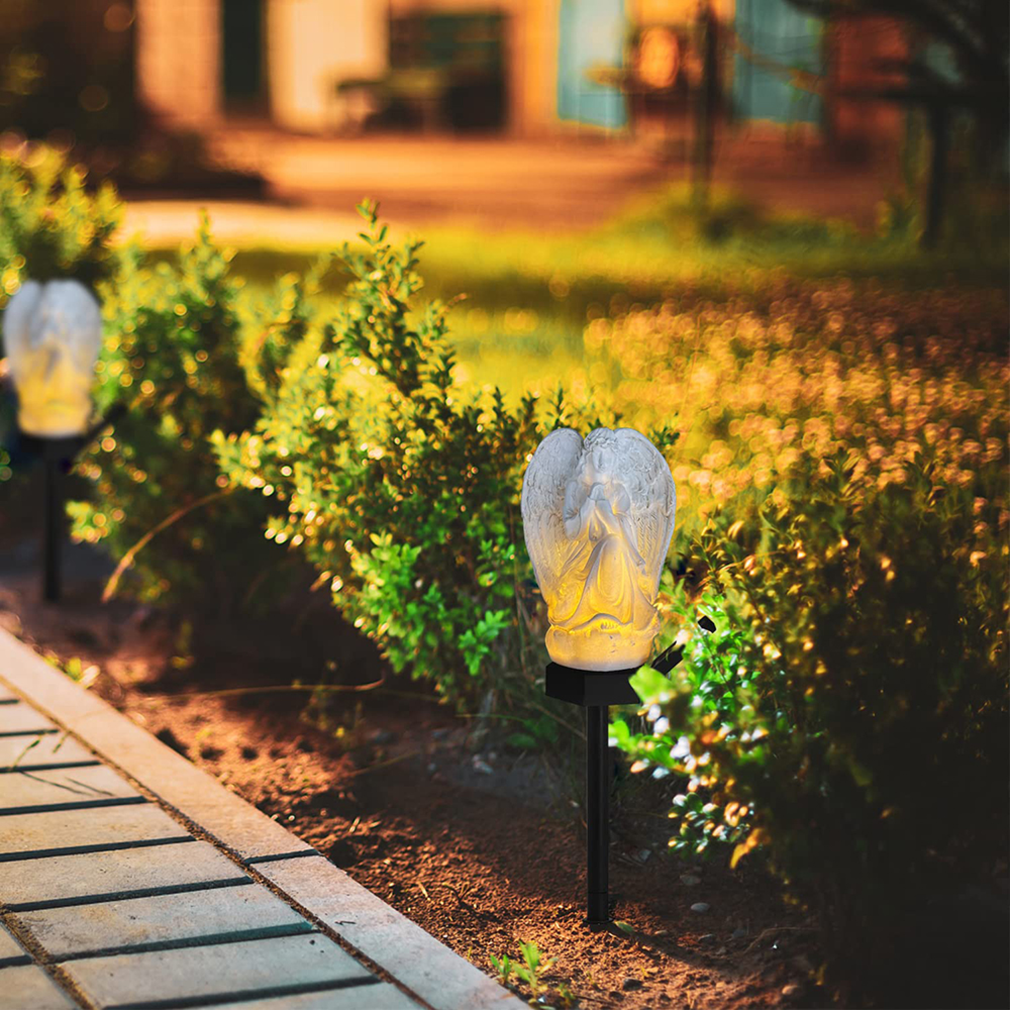 Zwei Engel-Solarleuchten beleuchten einen Gartenweg mit Büschen im Hintergrund.