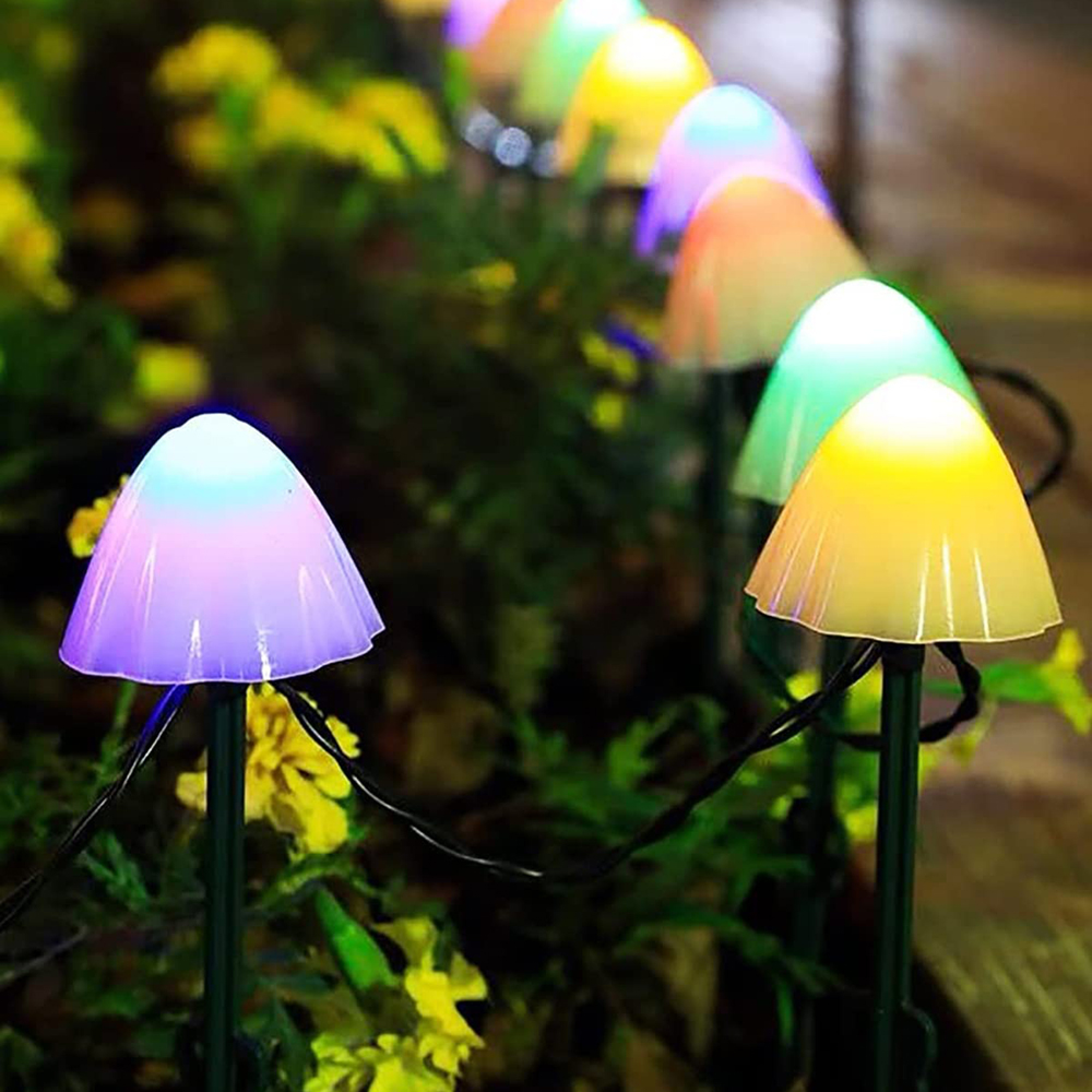 Bunte Pilz-Lichterkette in einem Garten mit gelben Blumen.