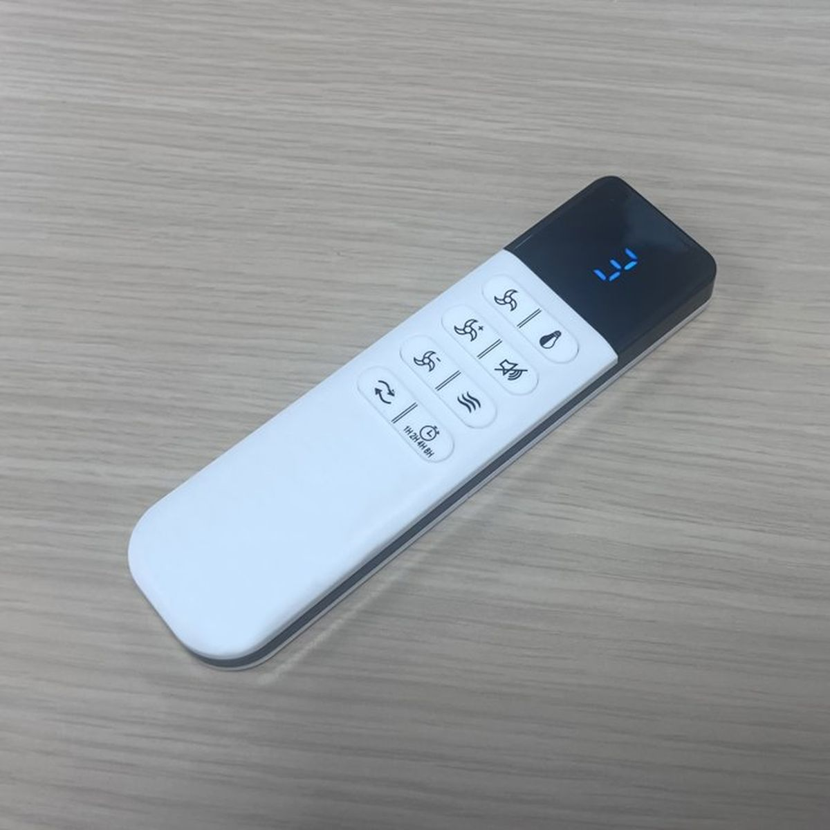 Een witte afstandsbediening met zwarte knoppen en een blauw digitaal display.