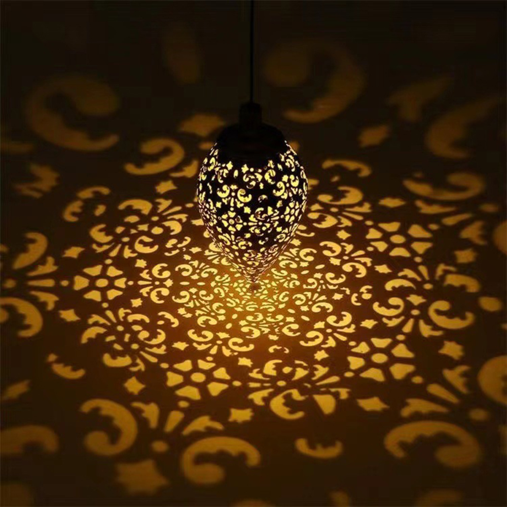 Eine verzierte Lampe projiziert ein Muster aus Licht und Schatten an eine Wand.