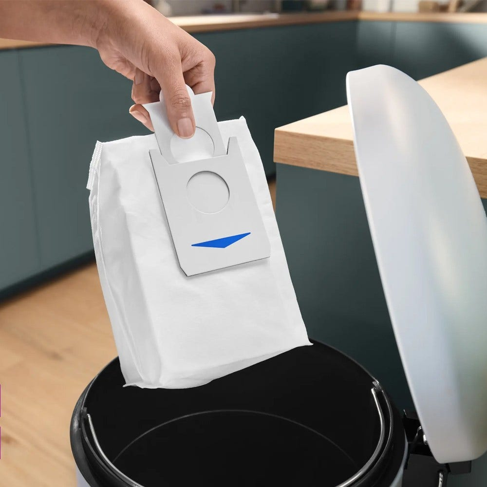 Eine Hand setzt einen weißen Staubsaugerbeutel in einen schwarzen Behälter ein.