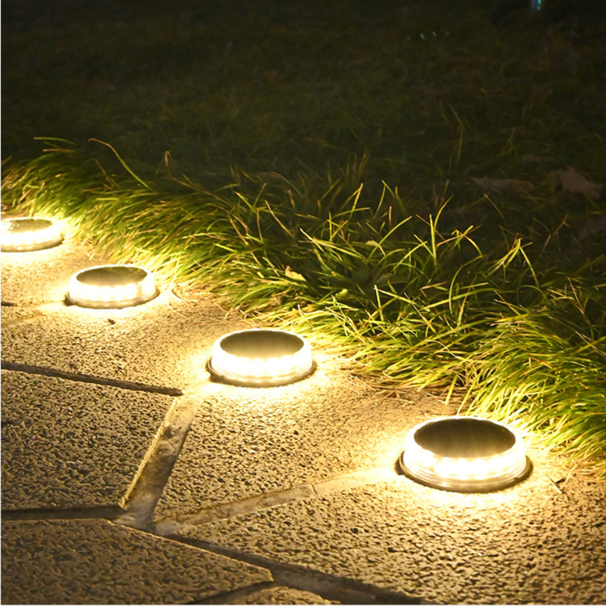 Bodenleuchten beleuchten einen Weg aus Steinplatten und Gras.