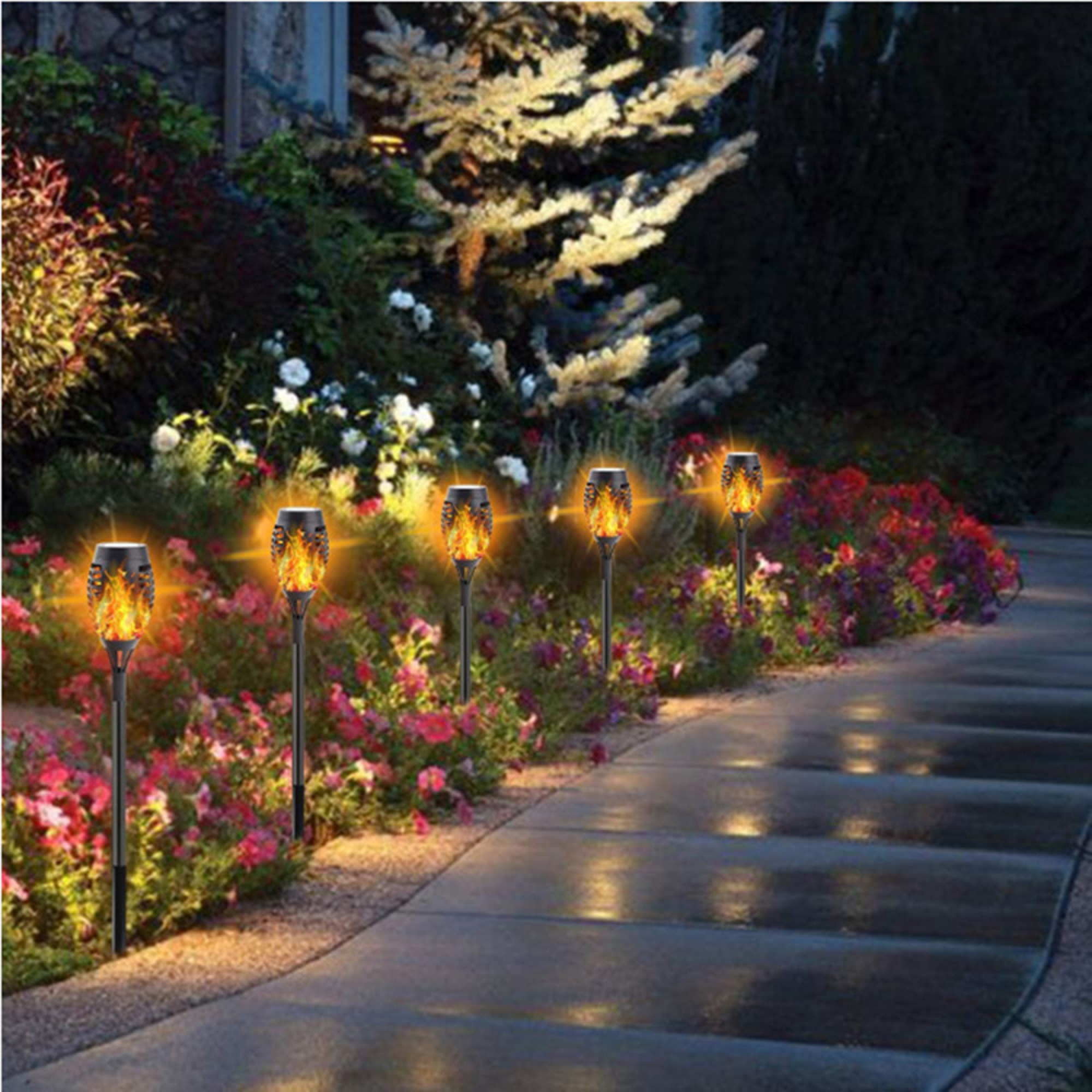 Gartenweg gesäumt von Solarflammenlichtern und bunten Blumen in der Dämmerung.