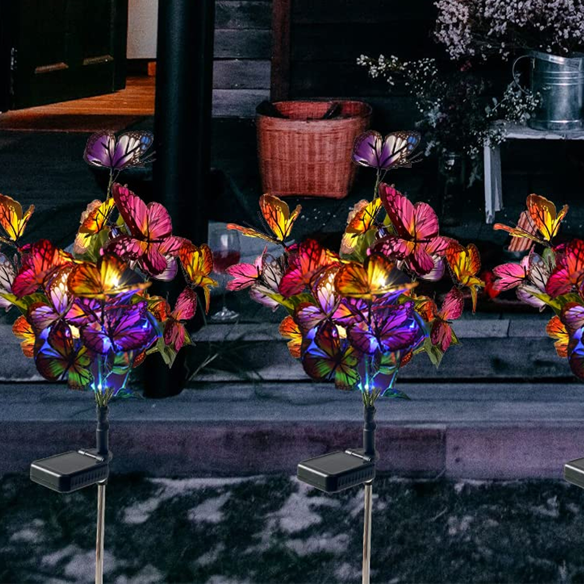 Bunte Schmetterlingslichter beleuchten eine dunkle Terrasse mit Korb und Weinglas.