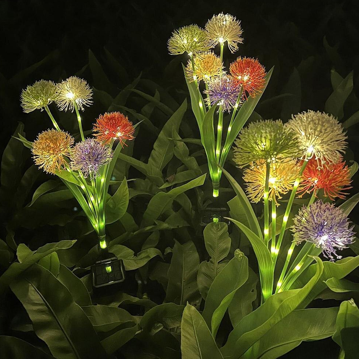 Beleuchtete Blumen-Solarleuchten in Orange, Lila, Gelb und Weiß auf dunklem Hintergrund.