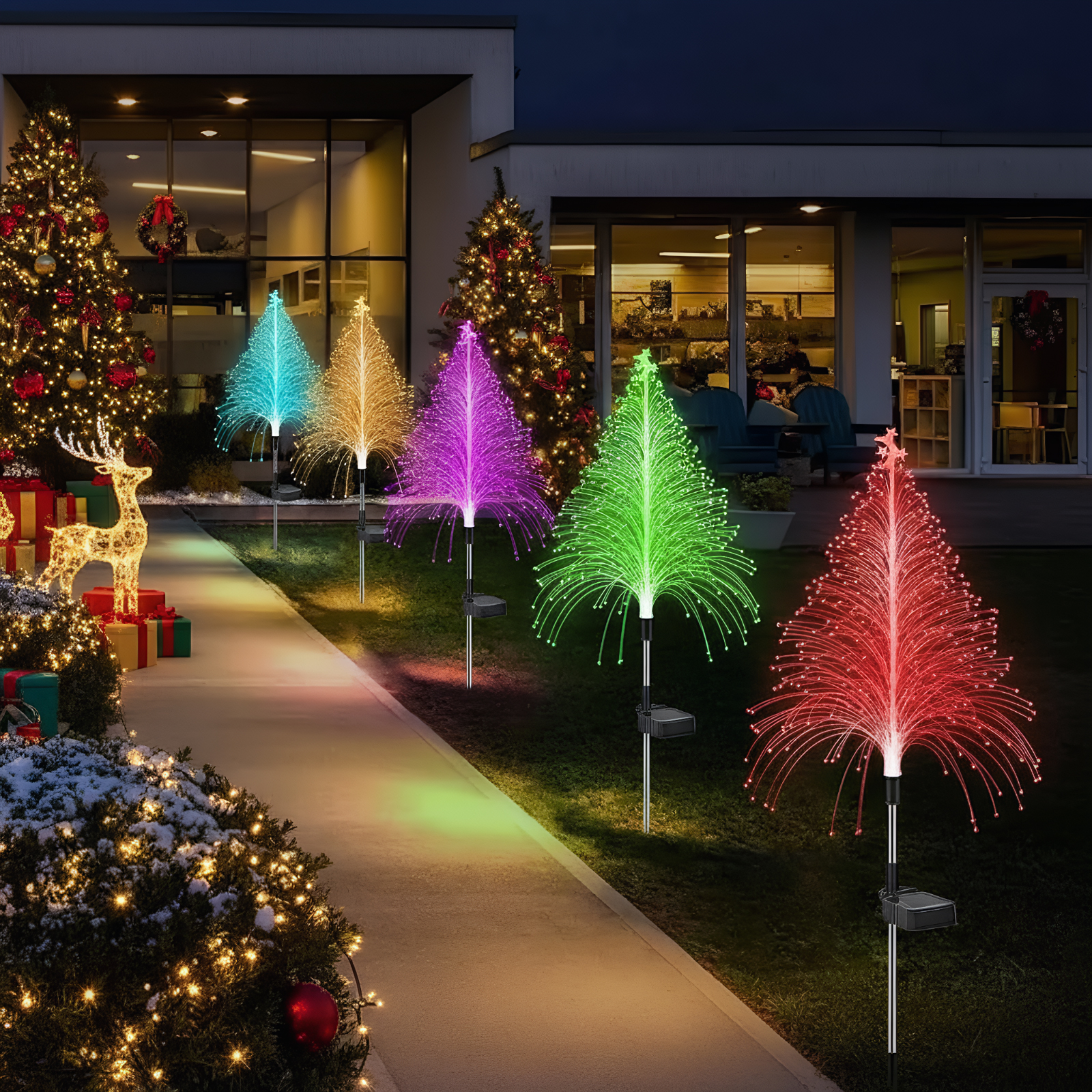 Bunte LED-Bäume beleuchten einen Gehweg vor einem Haus mit Weihnachtsbäumen.