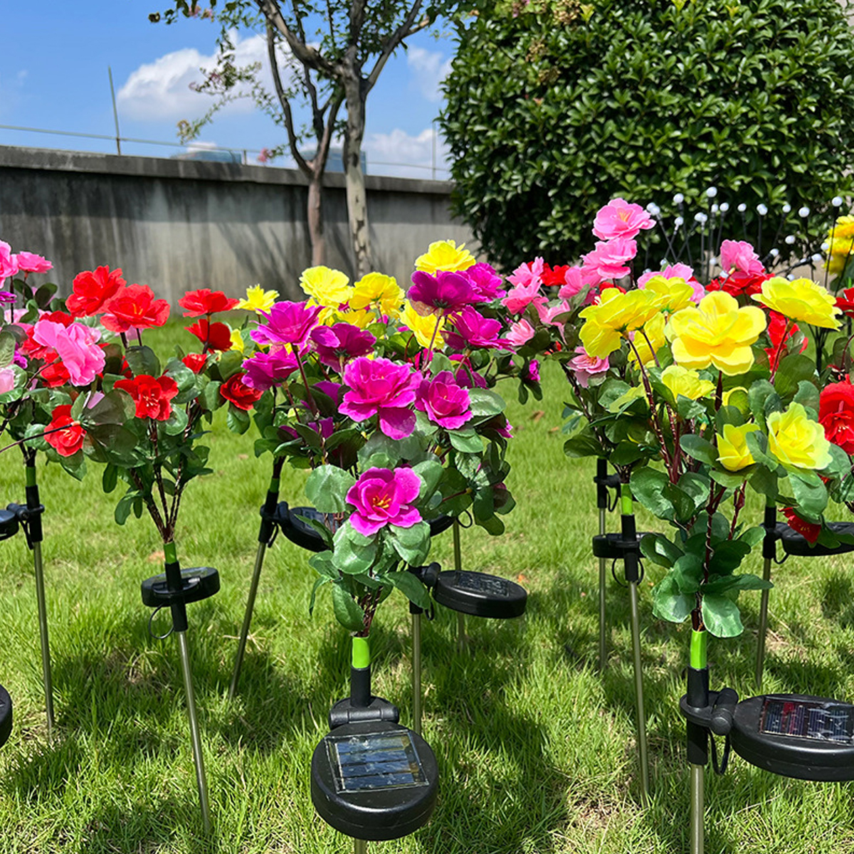 Bunte künstliche Blumen mit Solarlichtern auf Stöcken in grünem Gras.