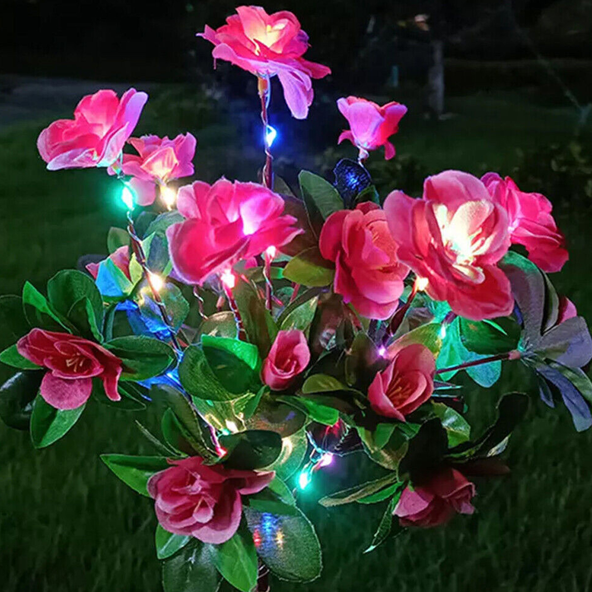 Rosa Blumen mit LED-Lichtern bei Nacht auf dunklem Gras.
