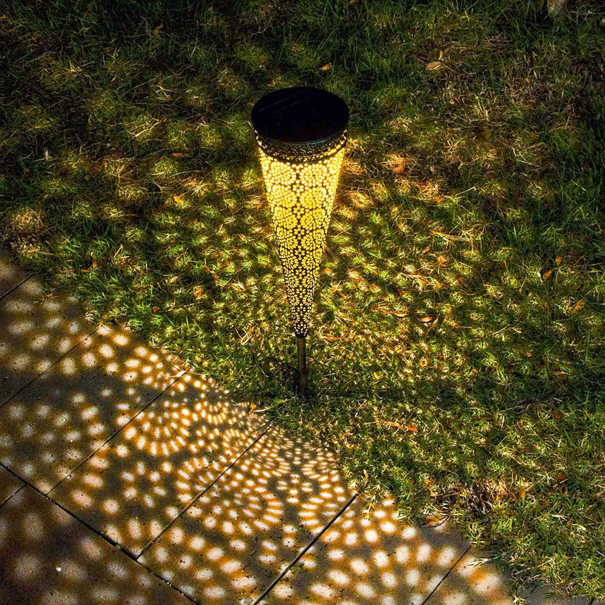 Beleuchtete Solarleuchte mit Lochmuster wirft Schatten auf Gras und Pflaster.