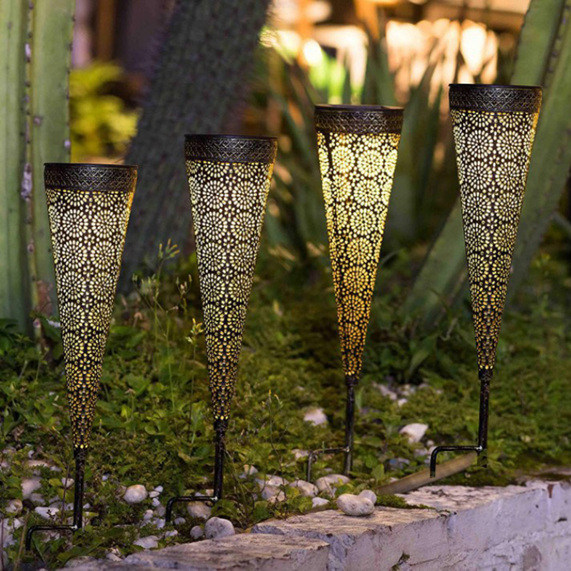 Vier verzierte Laternen beleuchten einen Gartenweg bei Nacht.