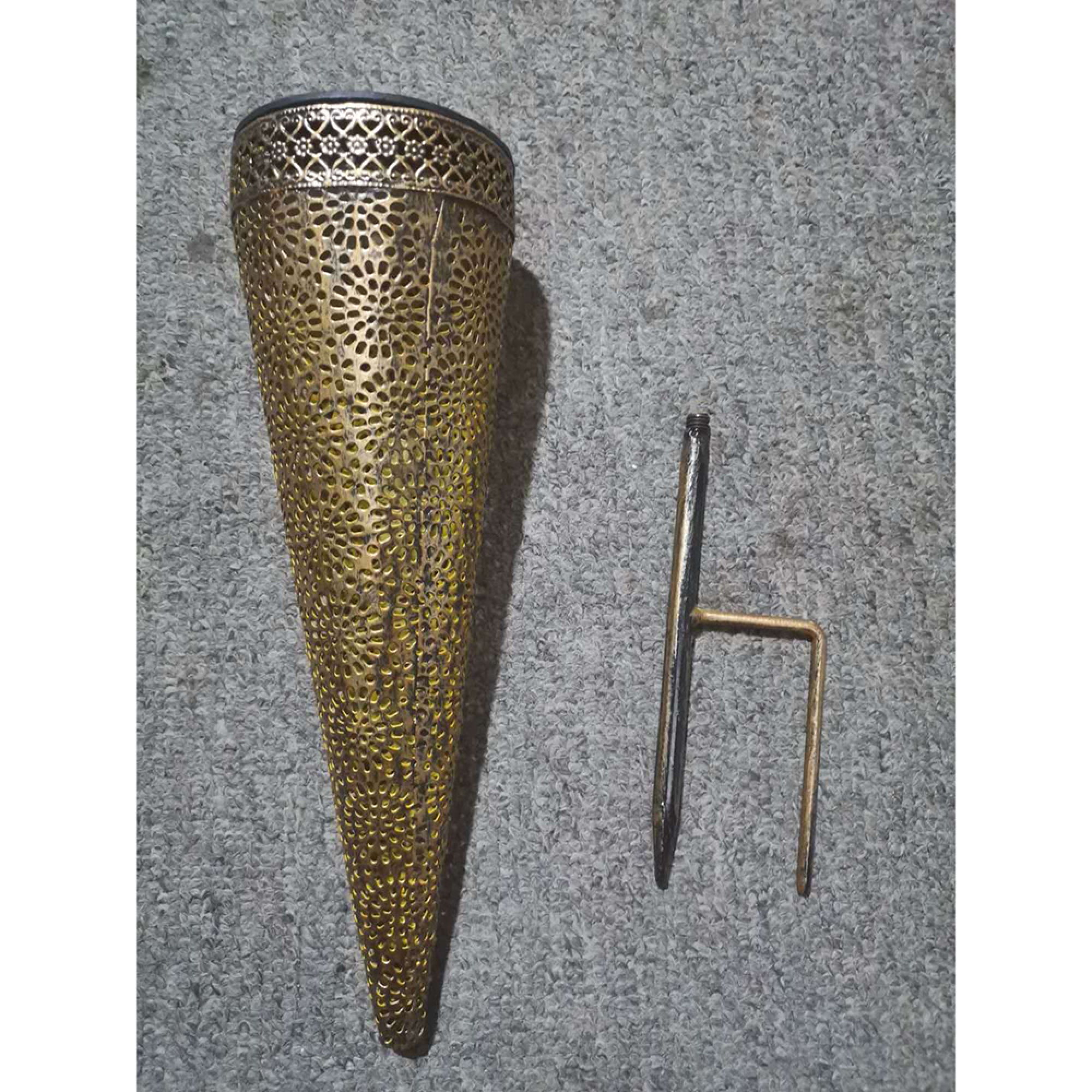 Goldene Lampe mit Lochmuster und Erdspieß auf grauem Teppich.