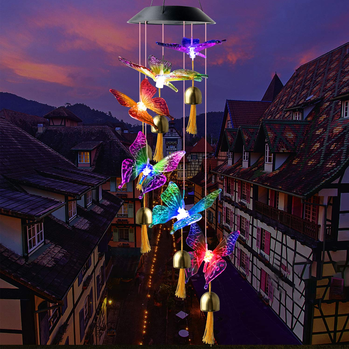 Solar-Schmetterlings-Windspiel mit bunten LED-Leuchten hängt über einer malerischen Straße in der Dämmerung.