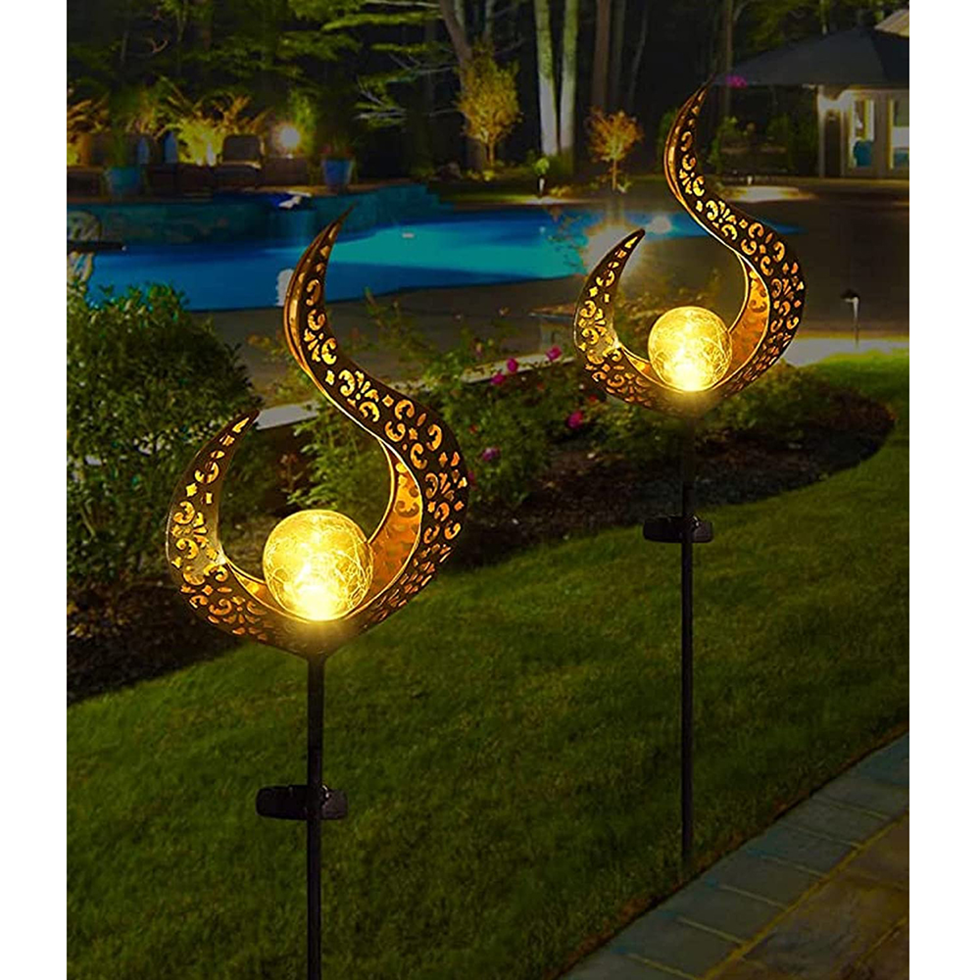 Zwei goldene Solarlampen mit geschwungenem Design und Glaskugeln auf einem Rasen.