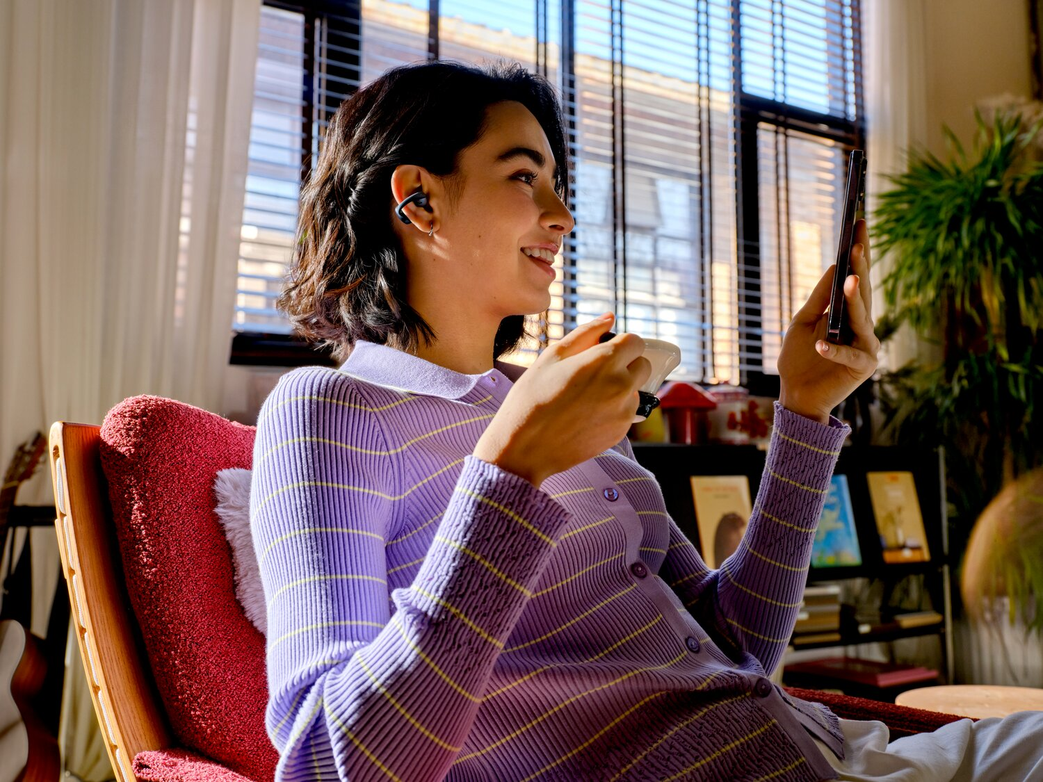 Una donna seduta su una poltrona rossa guarda il telefono e tiene una tazza.