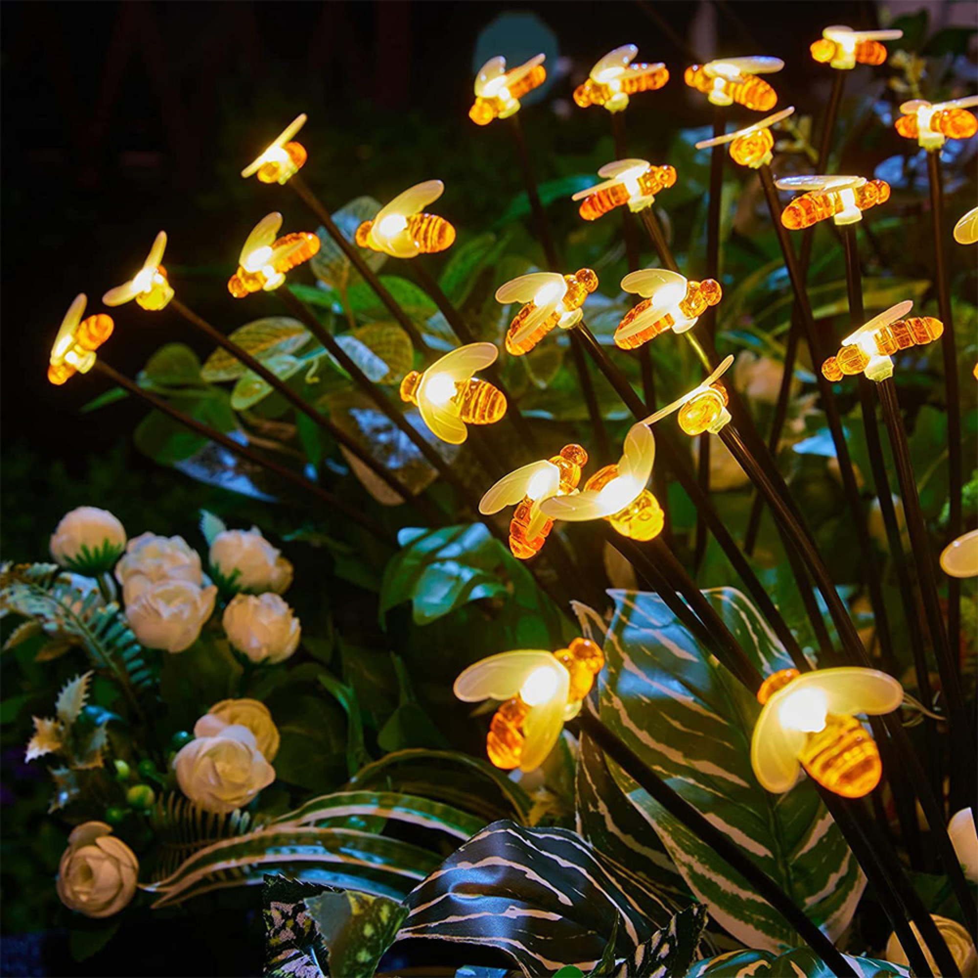 Beleuchtete bienenförmige Lichter zwischen grünem Laub und weißen Blumen.