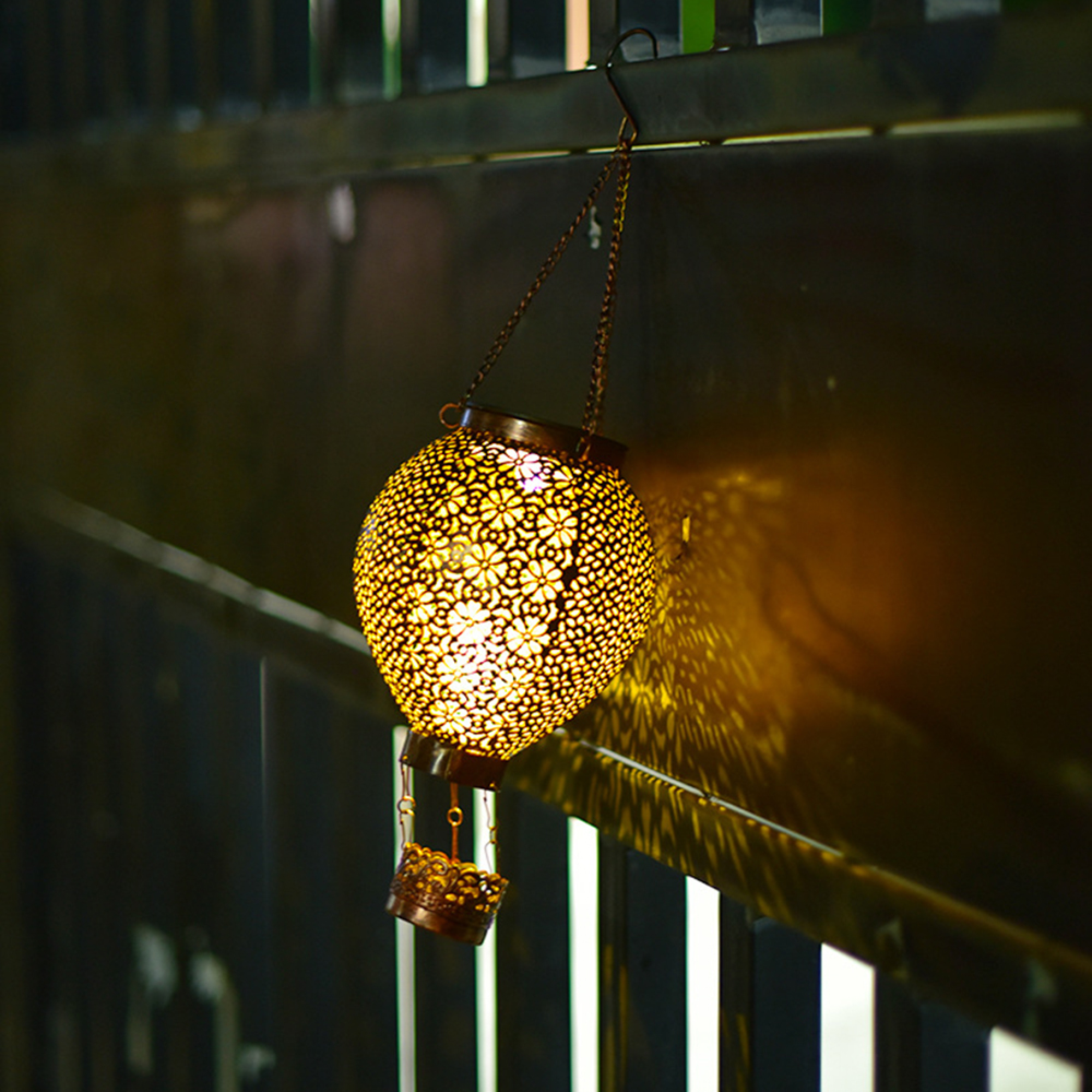 Eine verzierte goldene Laterne hängt an einer Kette und wirft gemusterte Schatten.