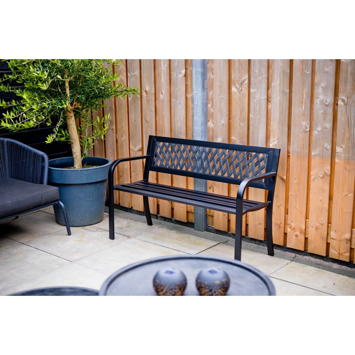 Zwarte tuinbank voor houten schutting met plantenbak en tafel.