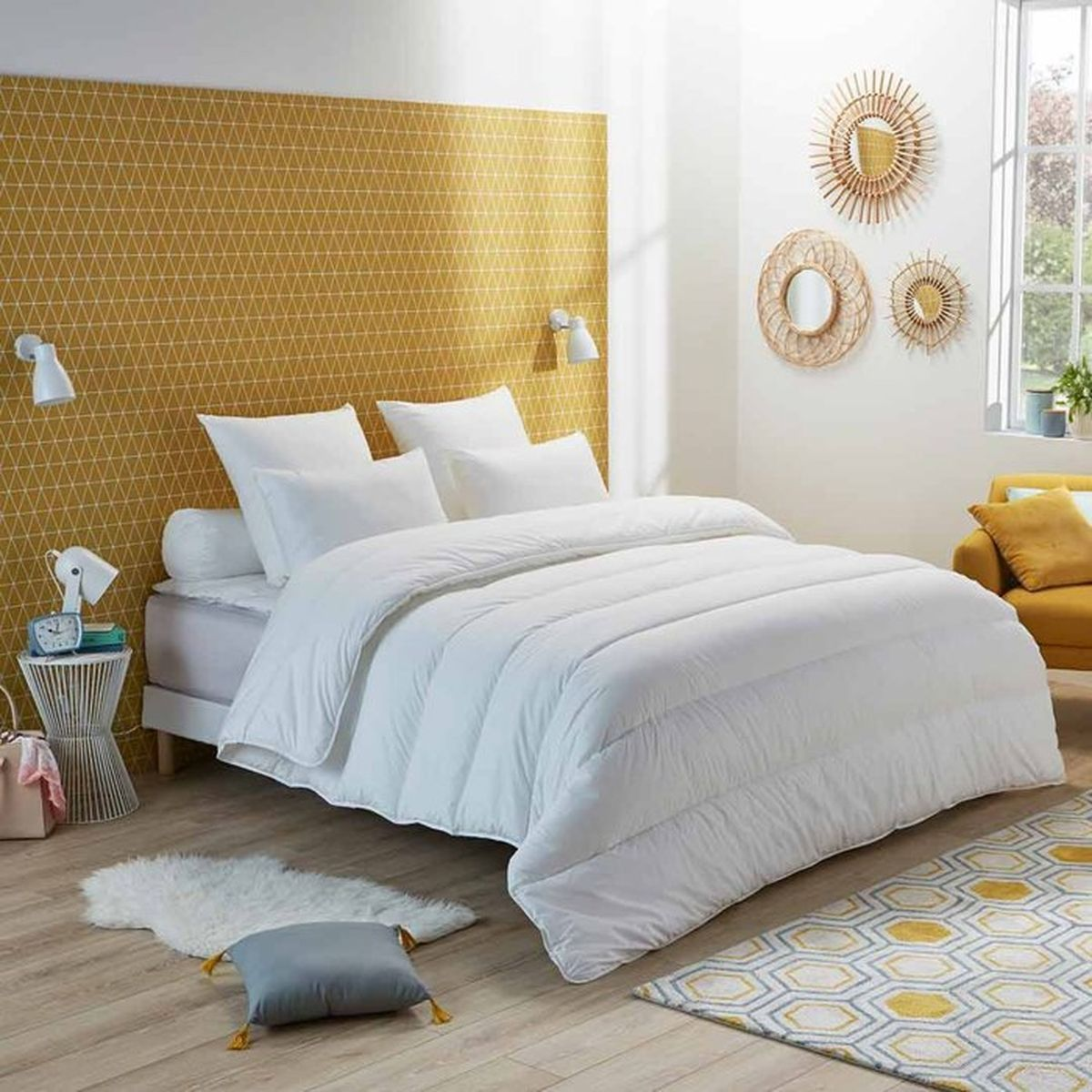 Ein Schlafzimmer mit einem weißen Bett, gelber geometrischer Tapete und Sonnenlicht.