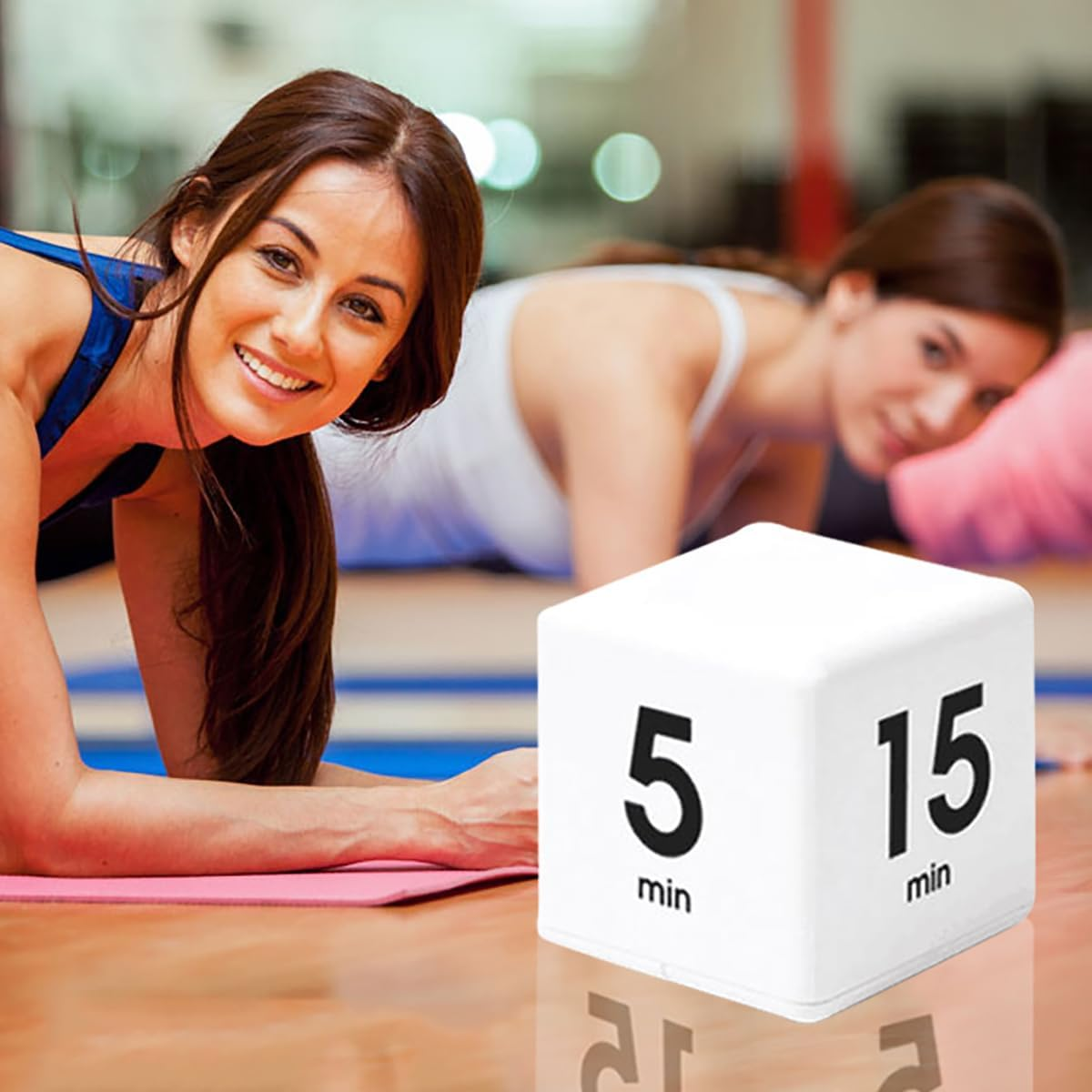 Zwei Frauen machen Liegestütze in einem Fitnessstudio, ein Timer liegt vorne.