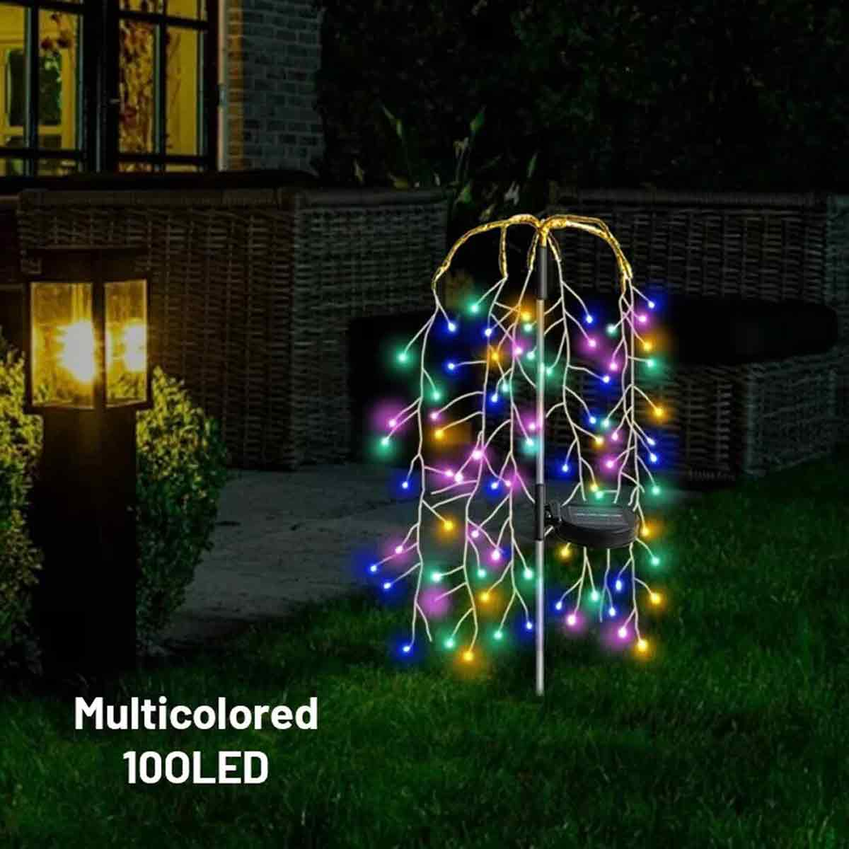 Eine mehrfarbige LED-Trauerweide-Lichtdekoration steht nachts auf einem Rasen.