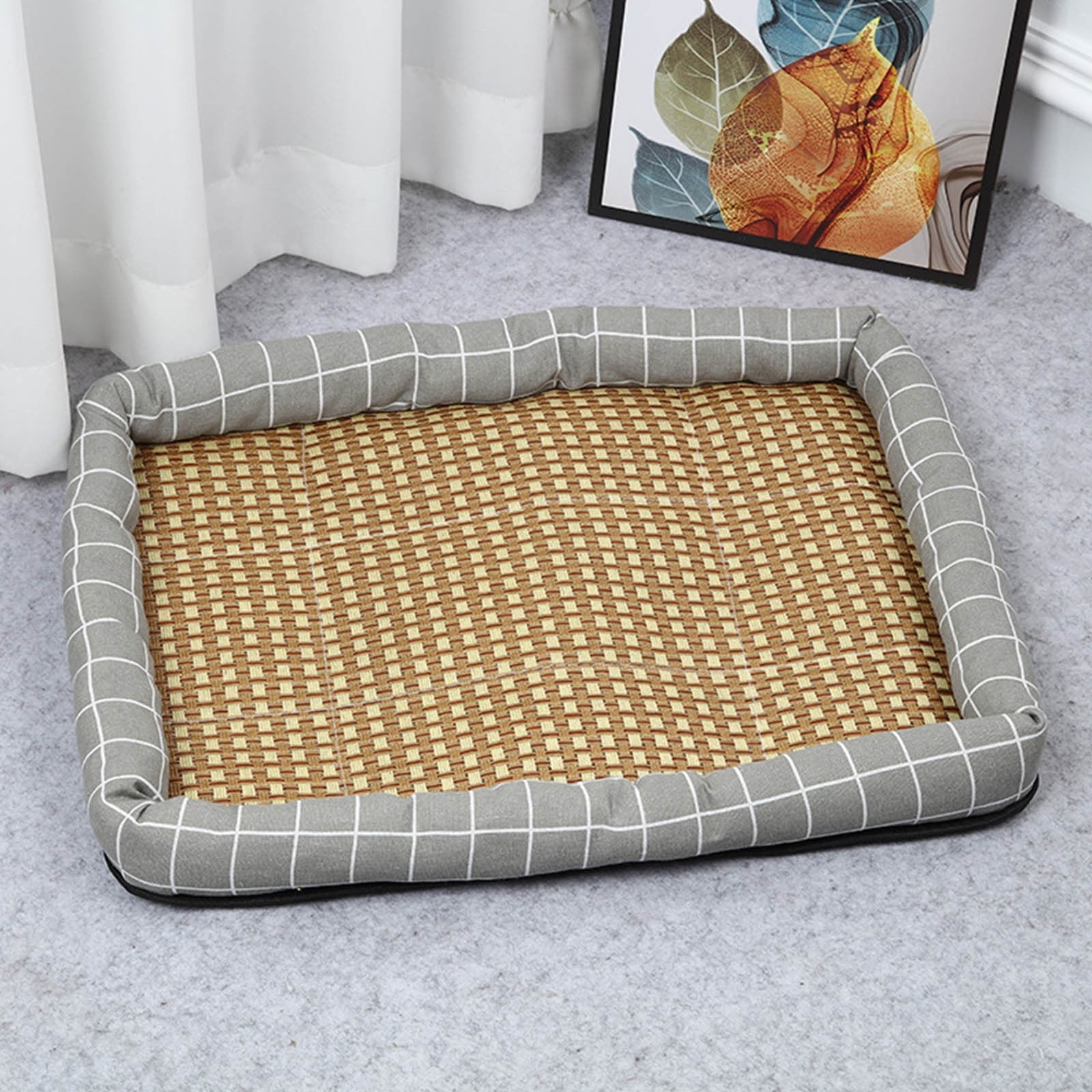 Ein rechteckiges Haustierbett mit kariertem Rand und Rattan-Einlage auf grauem Teppich.