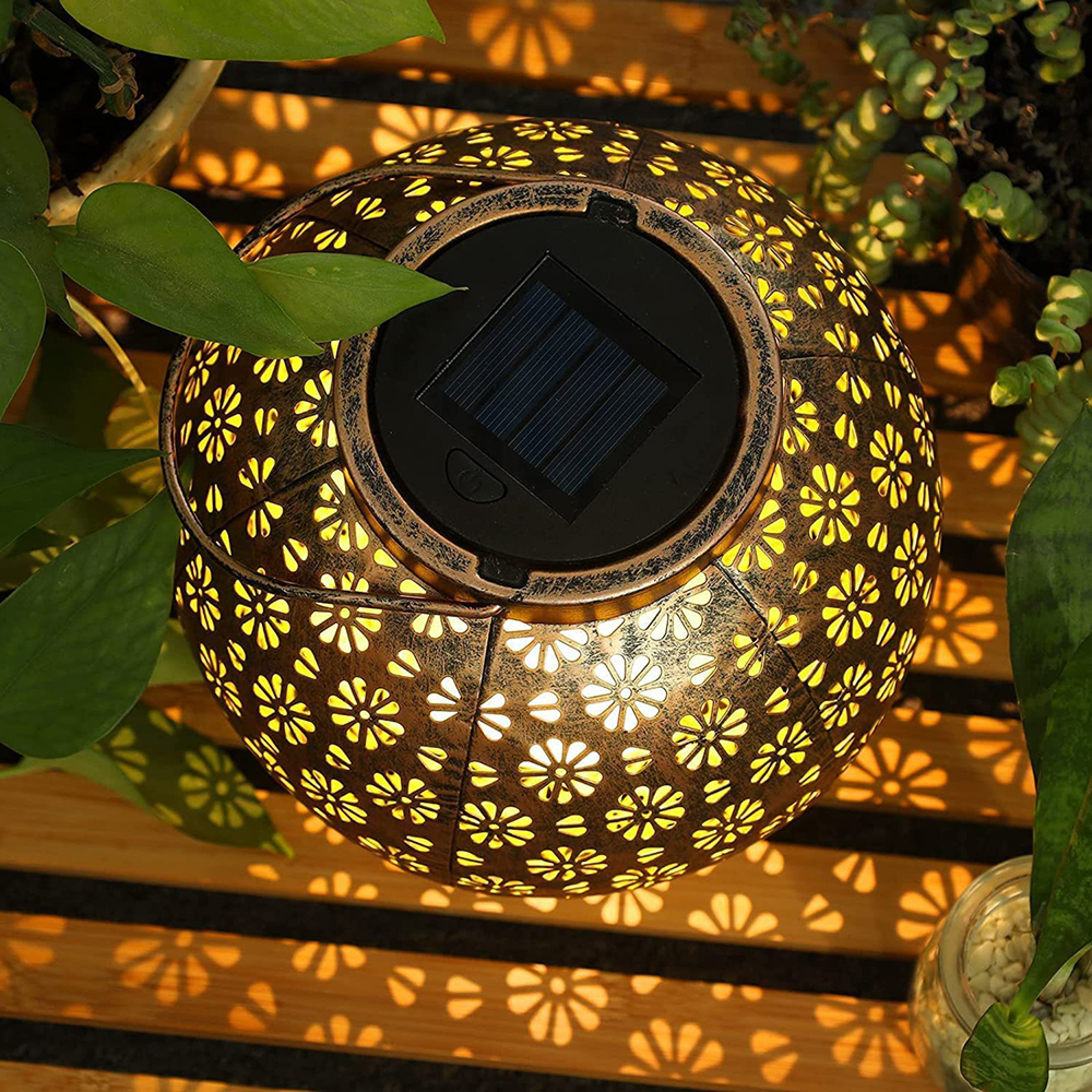 Eine bronzefarbene Solarlaterne mit Blumenmuster leuchtet auf einem Holzsteg.