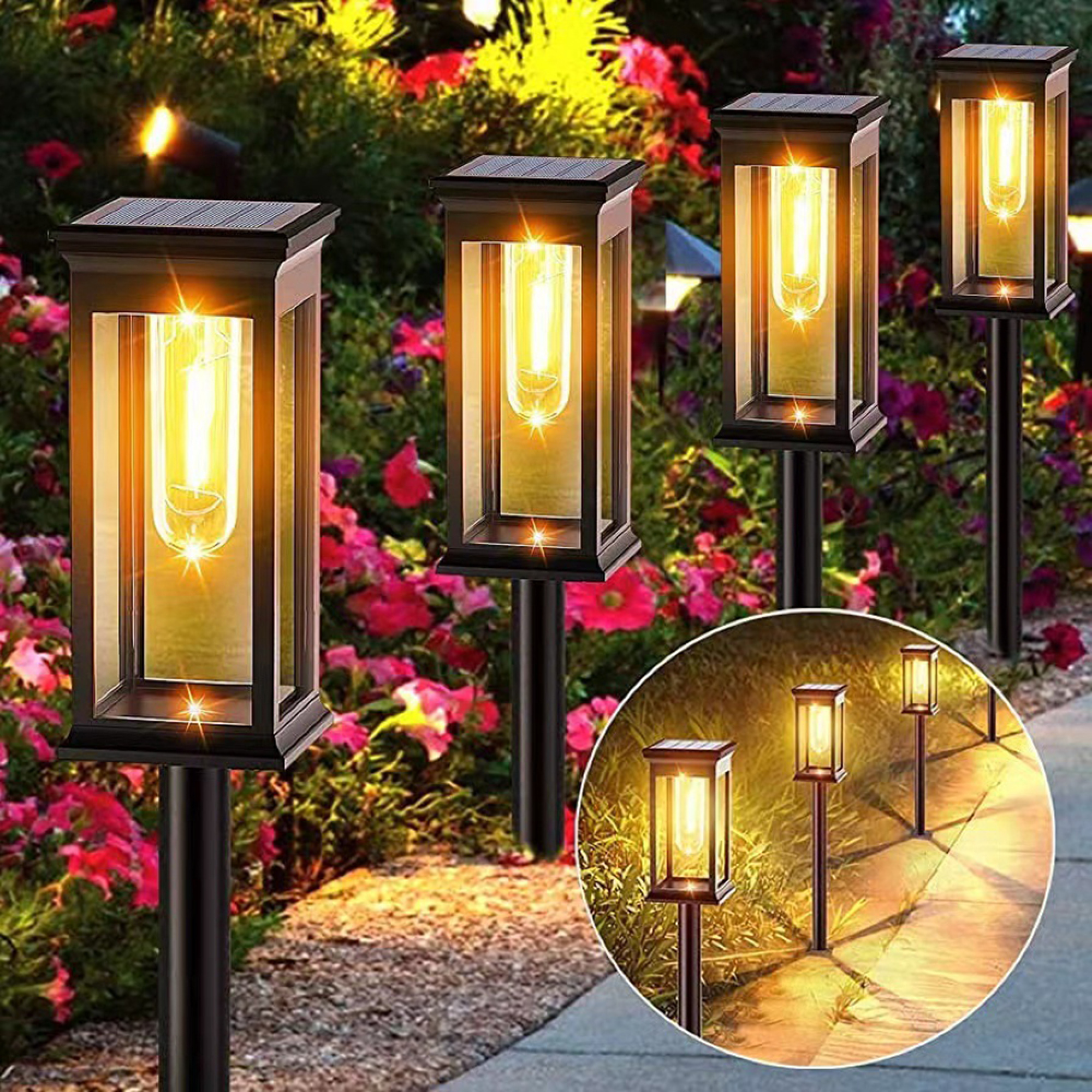 Gartenleuchten mit Solarzellen beleuchten einen Weg zwischen blühenden Blumen.