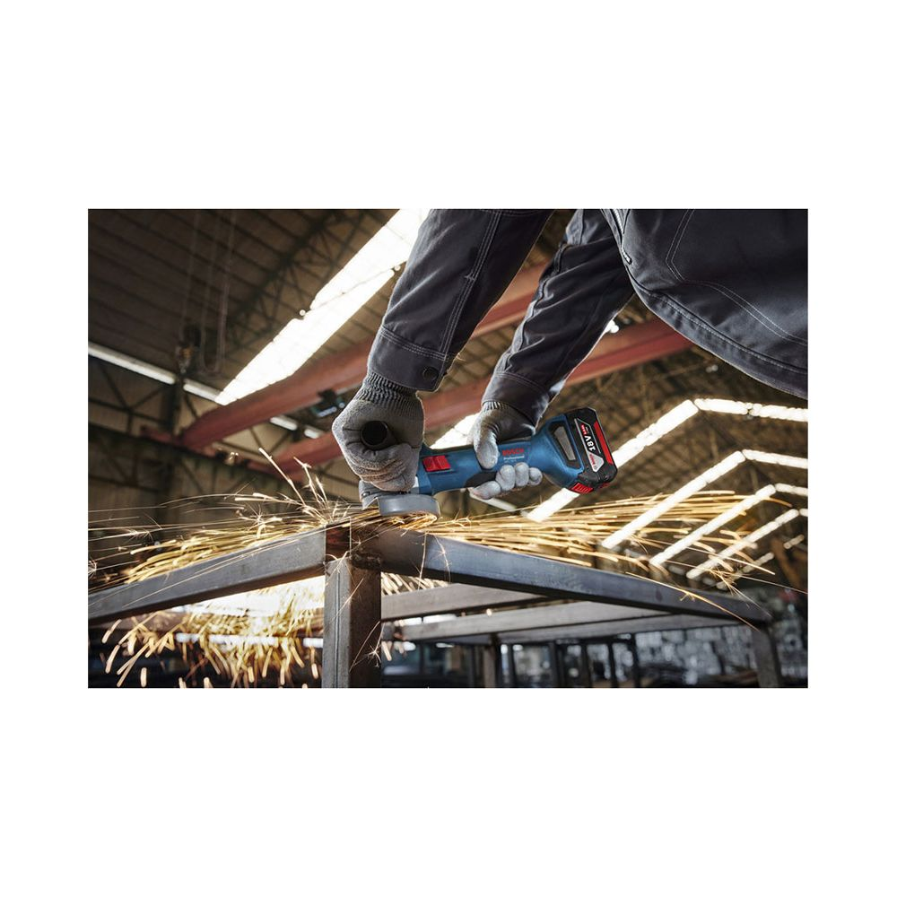 Ein Handwerker schleift Metall mit einem blauen Winkelschleifer in einer Fabrikhalle.