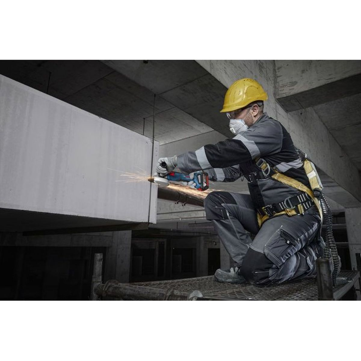 Mann mit Helm und Schutzmaske schleift mit Winkelschleifer auf Baustelle.