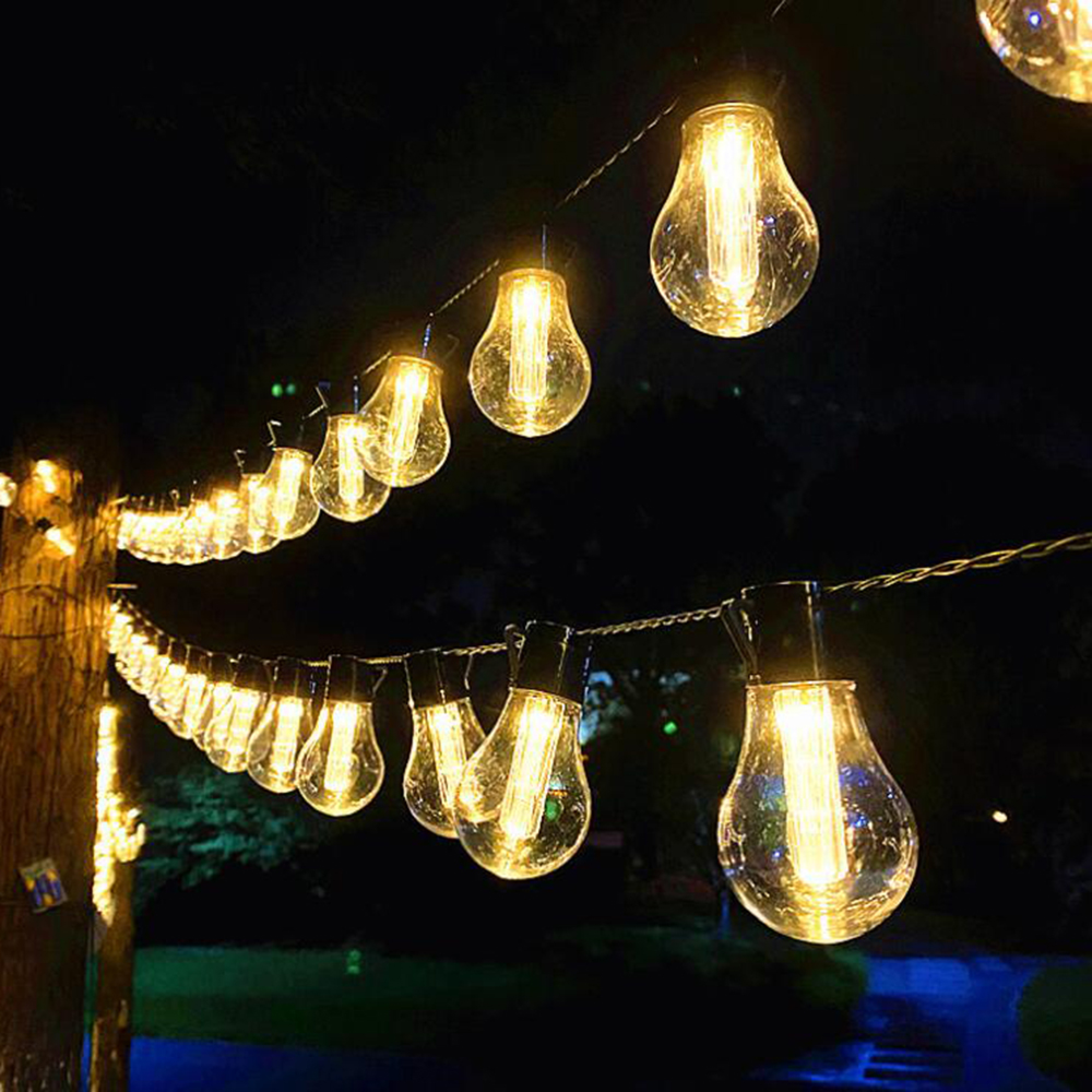 Lichterketten im Freien mit klaren Edison-Glühbirnen beleuchten eine dunkle Nachtszene.