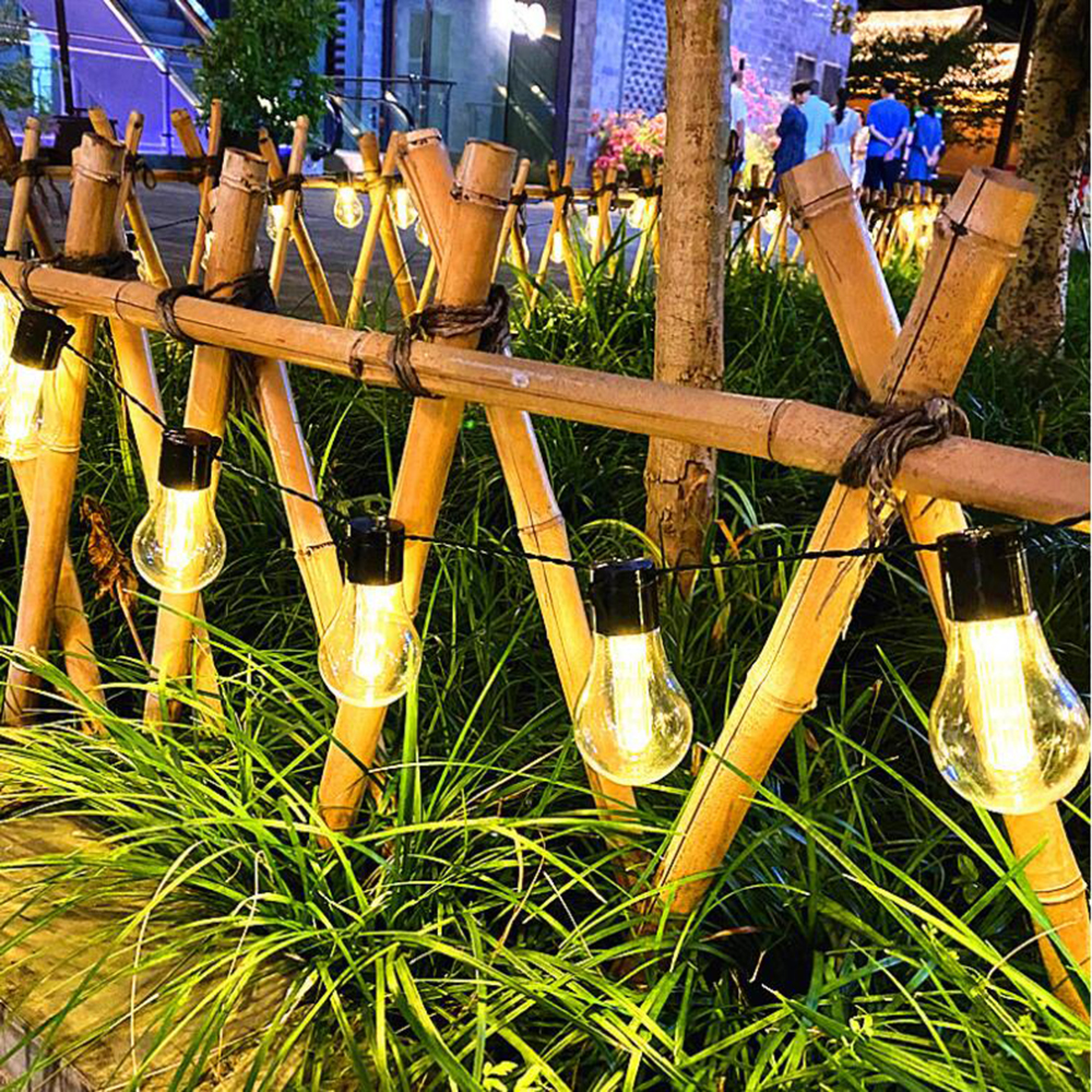 Beleuchteter Bambuzaun mit Glühbirnen im Gras bei Nacht.