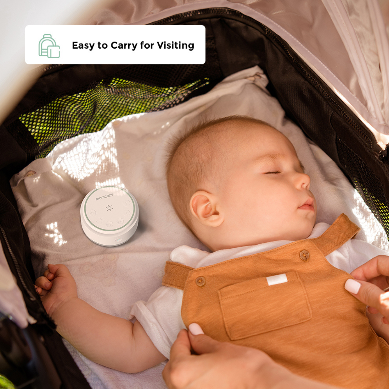 Een slapende baby in een kinderwagen met een witte geluidsmachine ernaast.